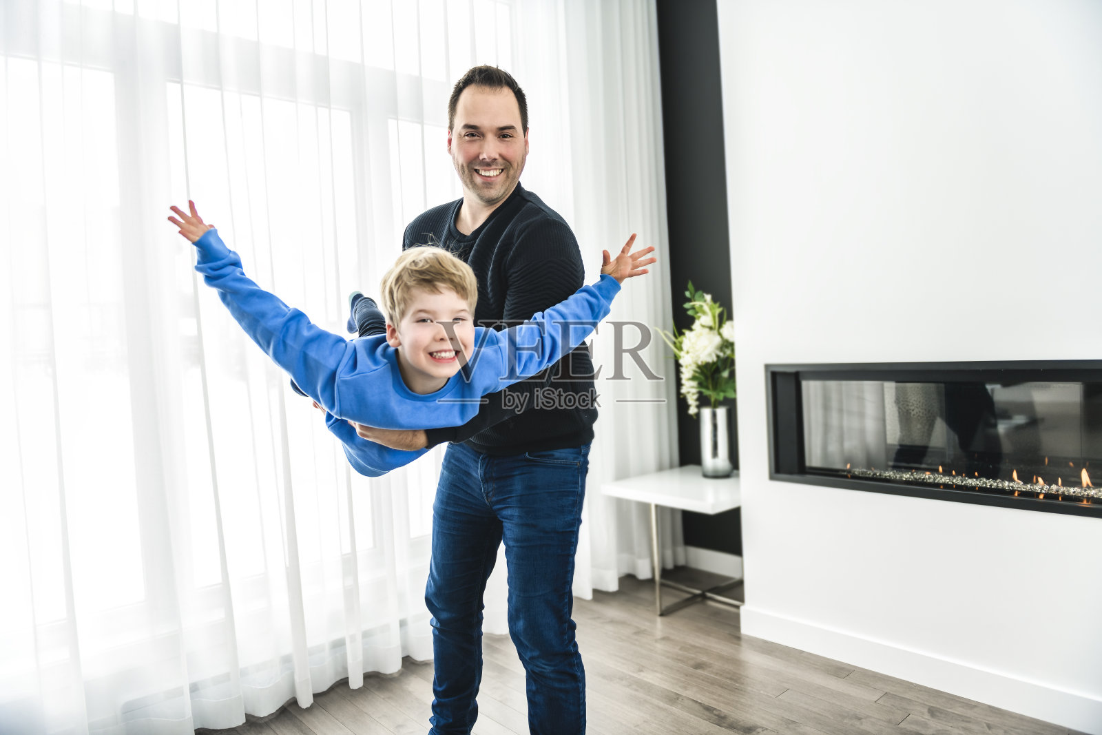 爸爸和他可爱的小男孩在一个现代的房子在客厅玩飞机照片摄影图片