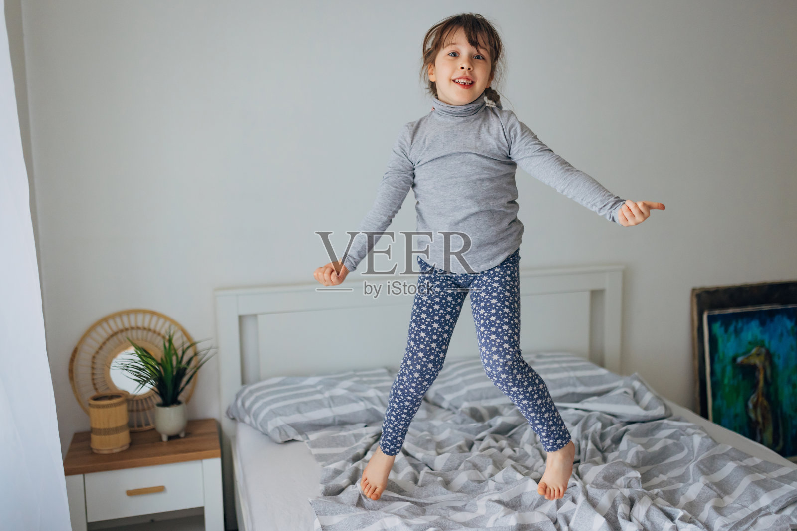 一个可爱的小女孩在明亮的卧室的床上跳得很开心。快乐童年概念照片摄影图片