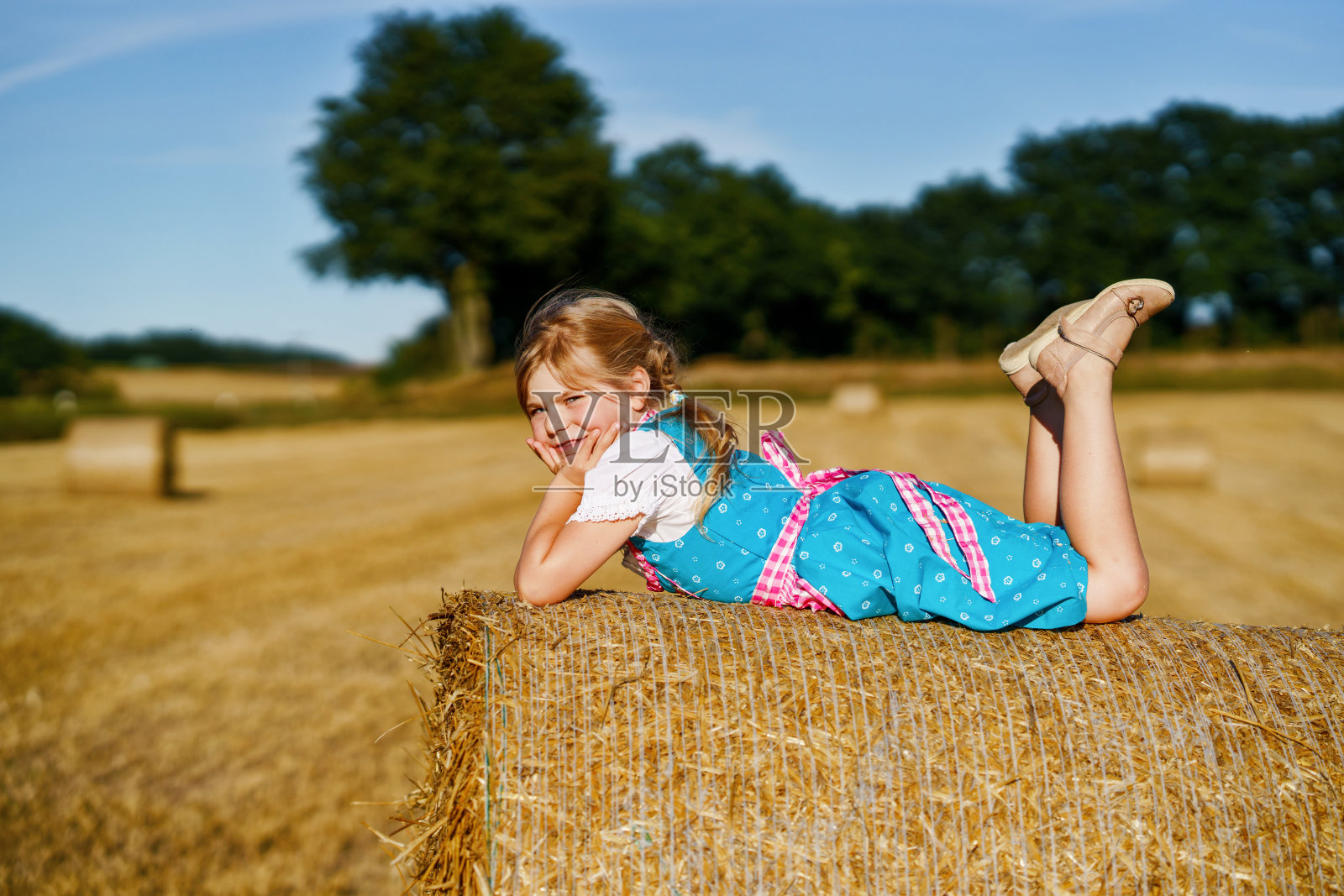 可爱的小女孩在传统的巴伐利亚服装在麦田。慕尼黑啤酒节期间,快乐的孩子拿着干草堆。德国夏季收获季节,学前班的女孩在干草堆上玩耍。照片摄影图片
