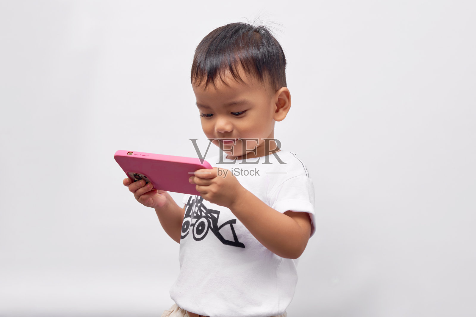 微笑有趣蹒跚学步的亚洲孩子男孩2岁穿着白色t恤使用手机玩游戏在线孤立在白色背景照片摄影图片