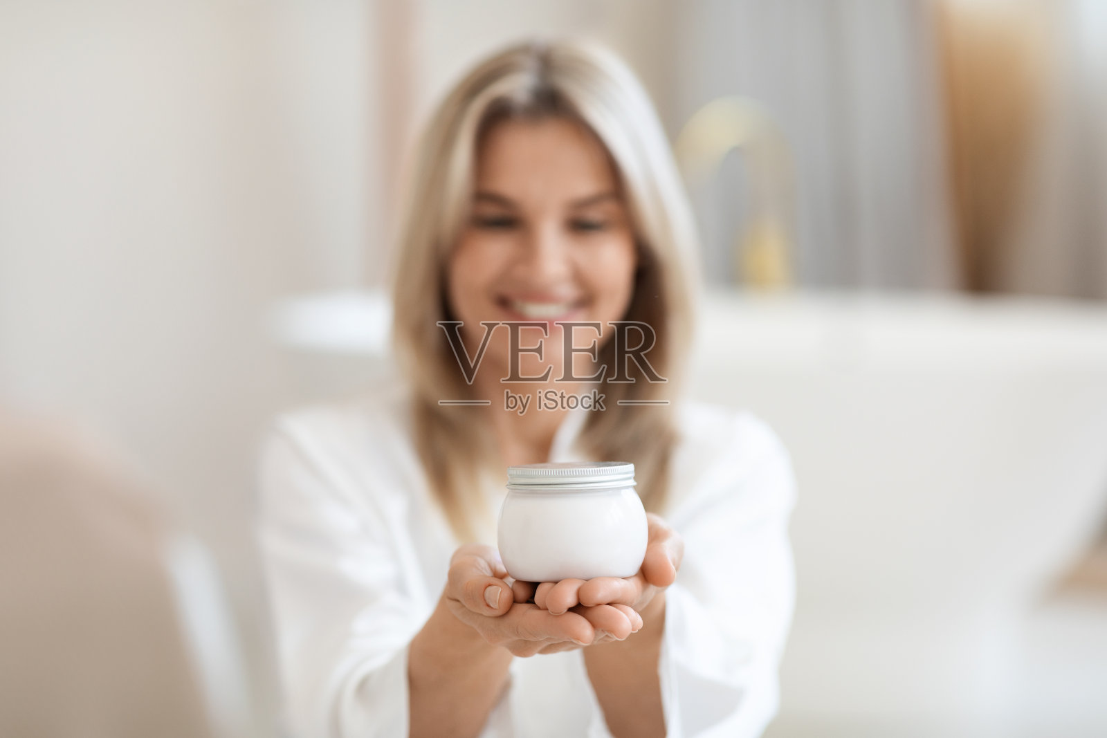 快乐的金发女人在浴袍使用身体护理产品照片摄影图片