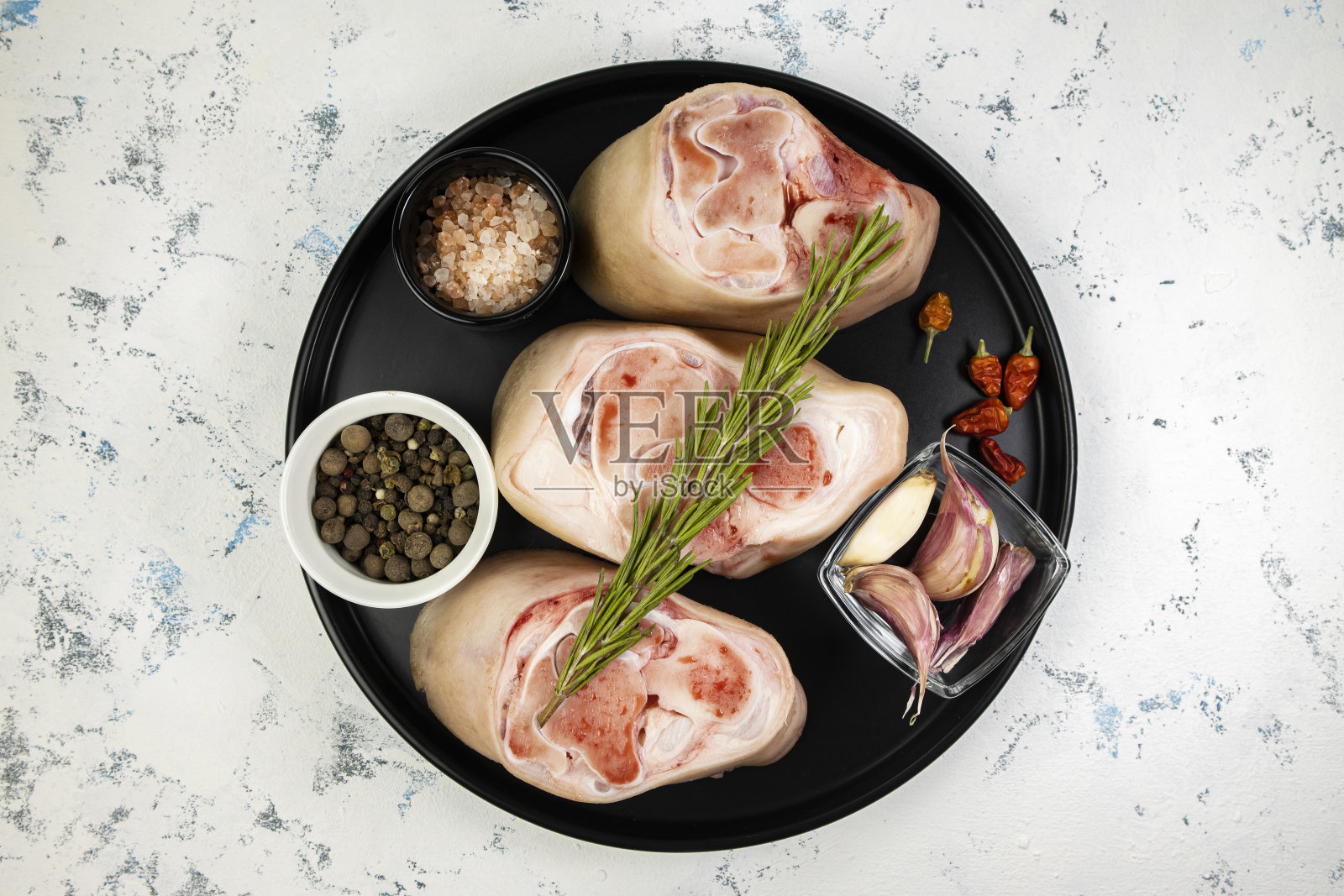 在抽象背景上的黑色盘子上调味的猪肉关节,俯视图,生猪肉照片摄影图片