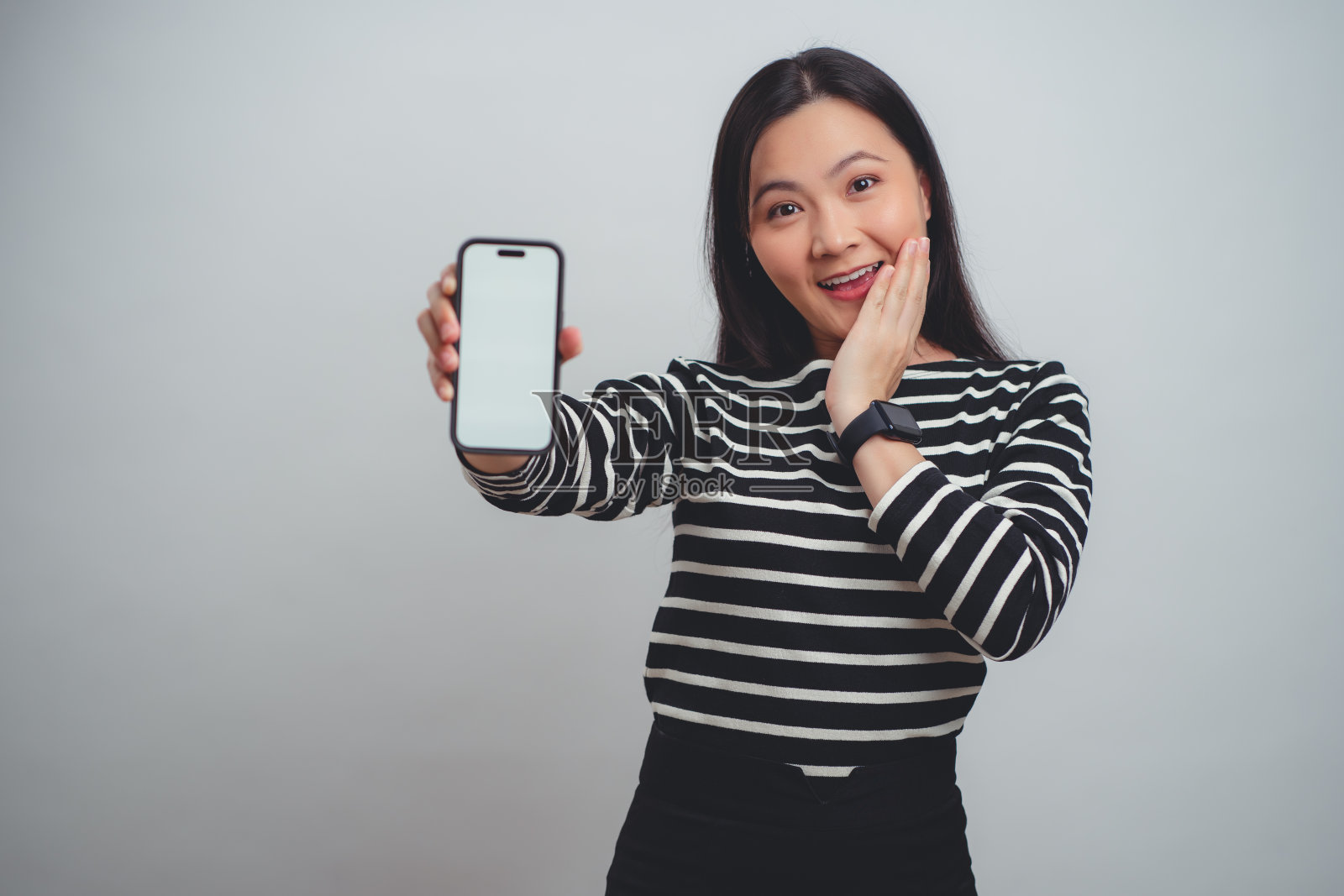 一名亚洲女性开心地笑着,智能手机上的白色屏幕孤立地站在白色背景上。照片摄影图片