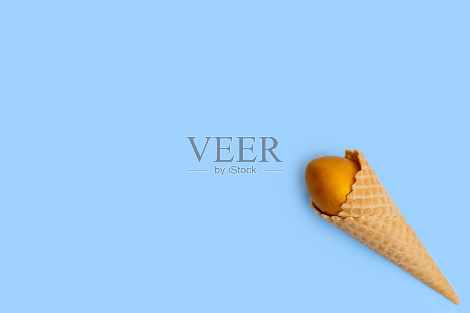 蓝色背景上装饰着金色复活节彩蛋的华夫冰淇淋蛋筒。照片摄影图片