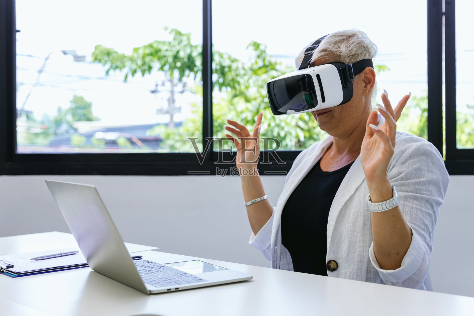 戴着VR头盔的商务女性。女子使用虚拟现实眼镜玩网络游戏。商务女性坐在带有安全接口的办公大楼内,使用虚拟现实耳机照片摄影图片