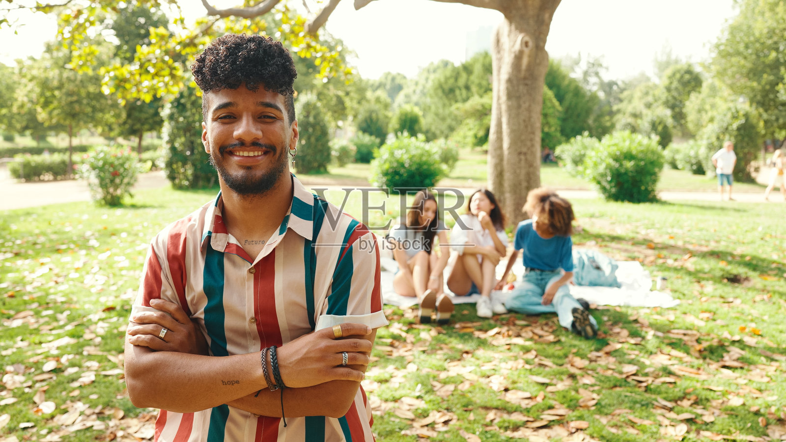 特写的年轻卷发男子穿着条纹衬衫坐在公园野餐的夏日户外,微笑着和朋友交谈照片摄影图片