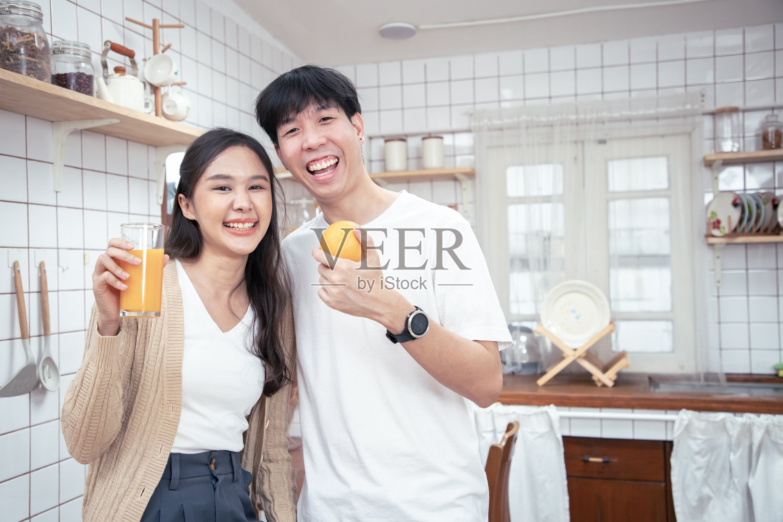 亚洲年轻夫妇在家里的现代厨房里享受新鲜的橙汁早餐。新家庭关系。健康的生活方式或有趣的竞赛概念照片摄影图片