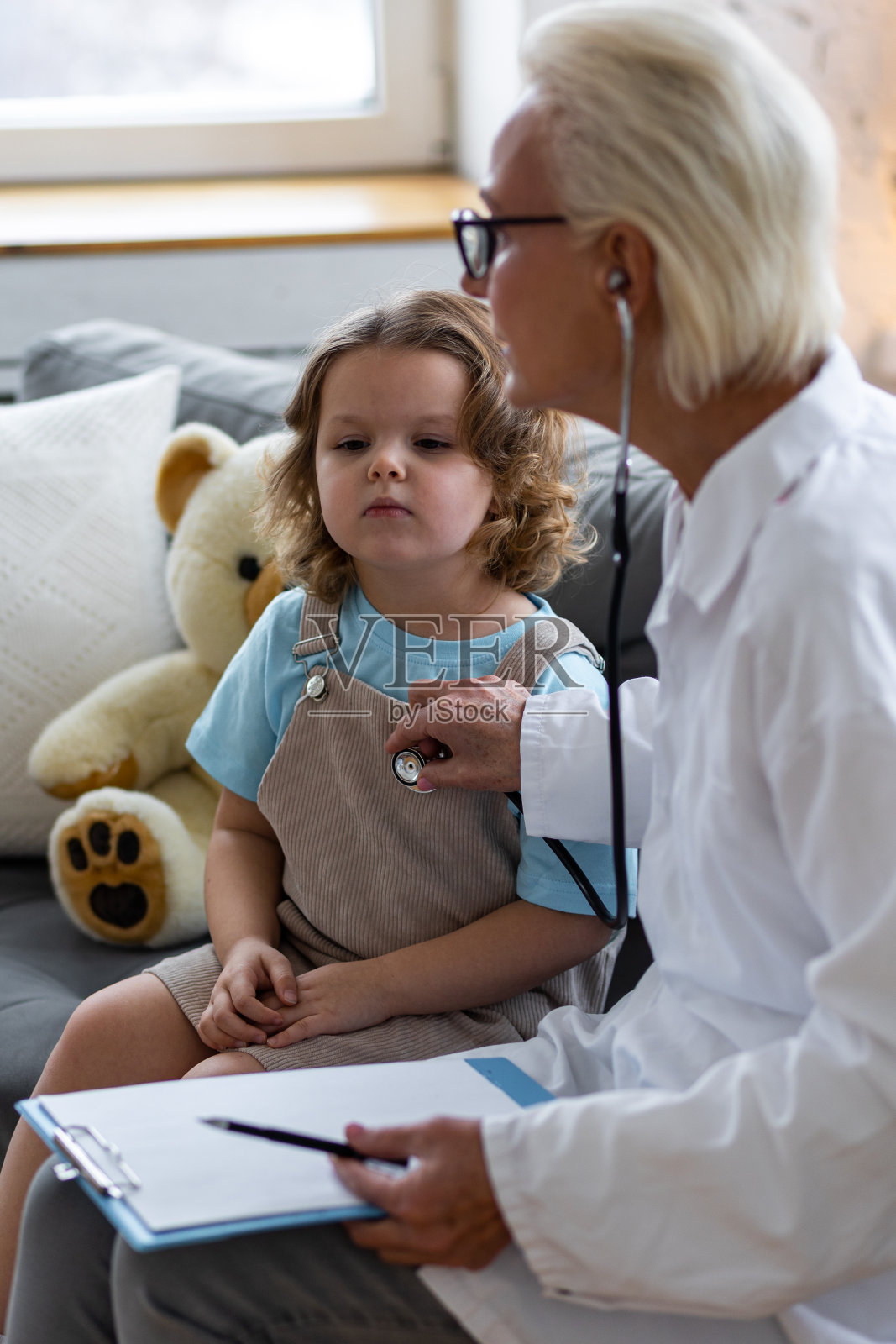 善良的女老年儿科医生到家里看望他的病人,检查小女孩,写处方。儿童健康检查的概念测量体温,心跳照片摄影图片