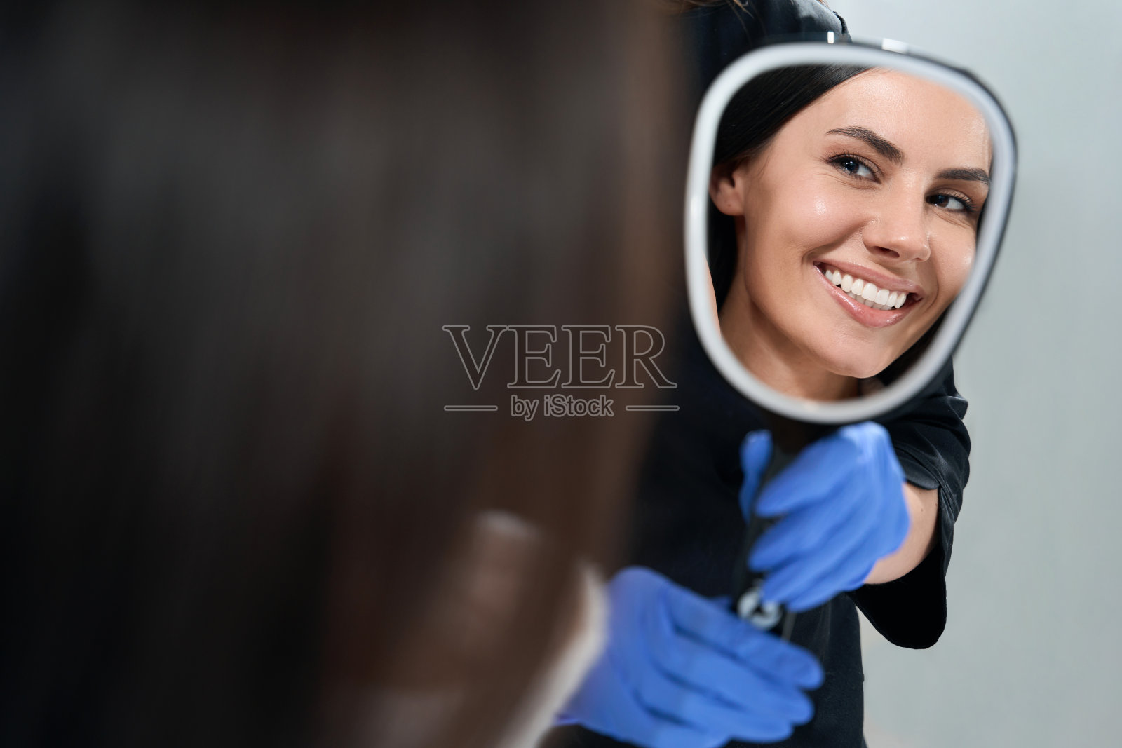 微笑的美丽女性在沙龙看着镜子照片摄影图片