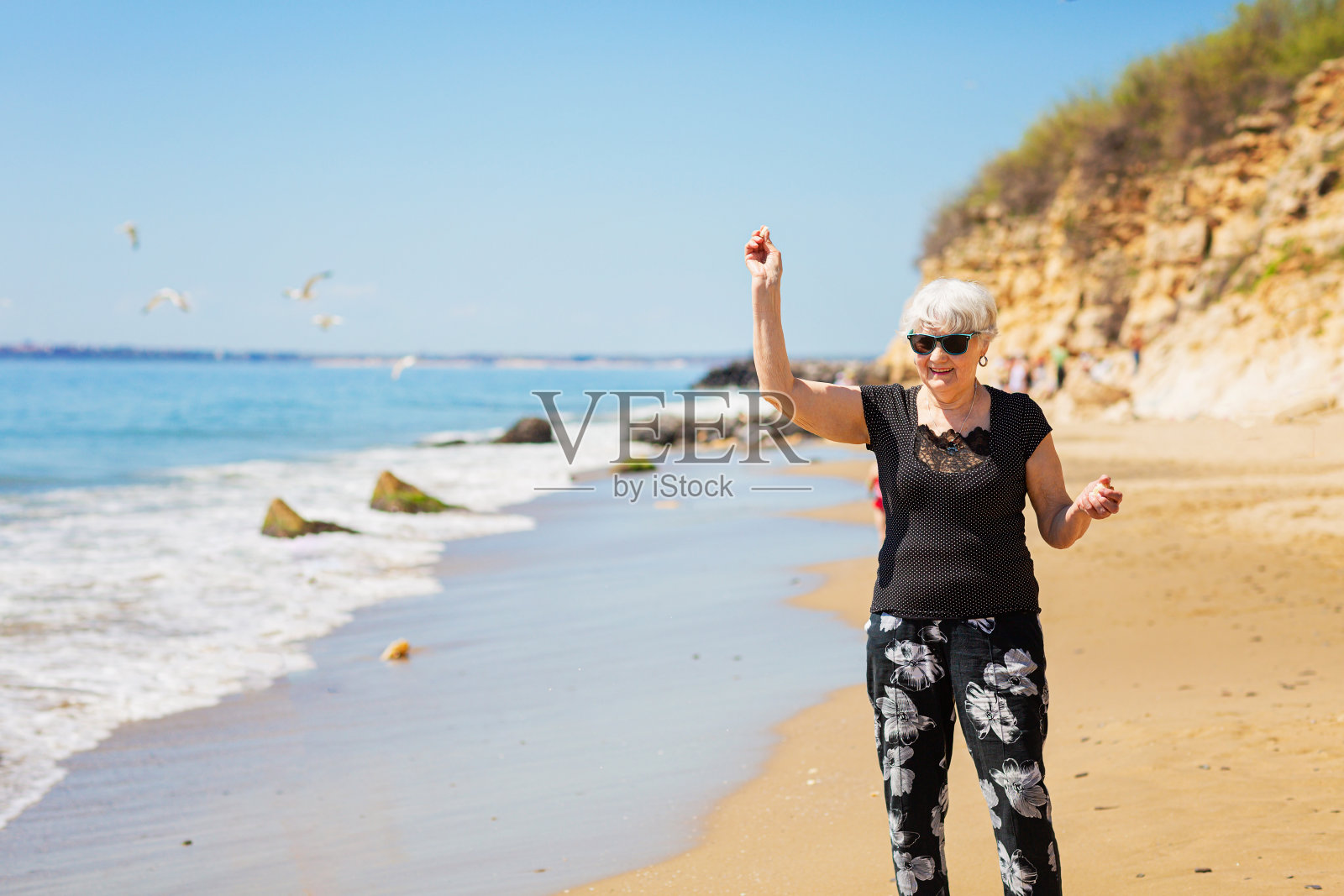 戴着墨镜的老妇人在海滩上喂海鸥照片摄影图片