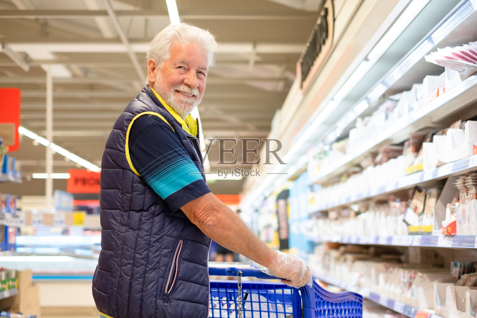 大胡子老人推着购物车在超市里买杂货,小心翼翼地考虑成本——消费主义的概念,价格上涨,通货膨胀照片摄影图片