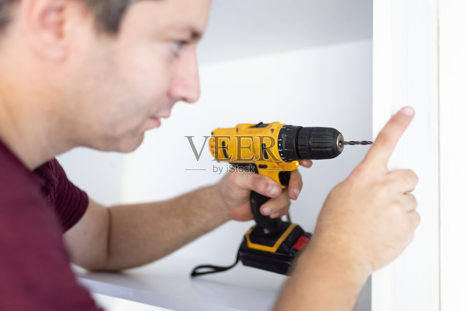 一名男子用无绳螺丝刀在家中组装白色厨房木制家具。拷贝空间。照片摄影图片