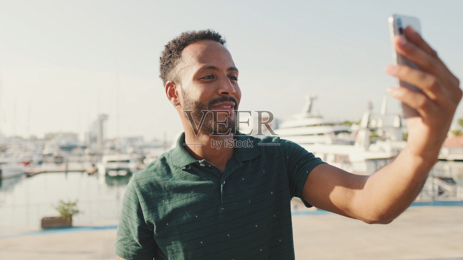 快乐的年轻人从电话视频电话,而坐在港口与游艇的背景照片摄影图片
