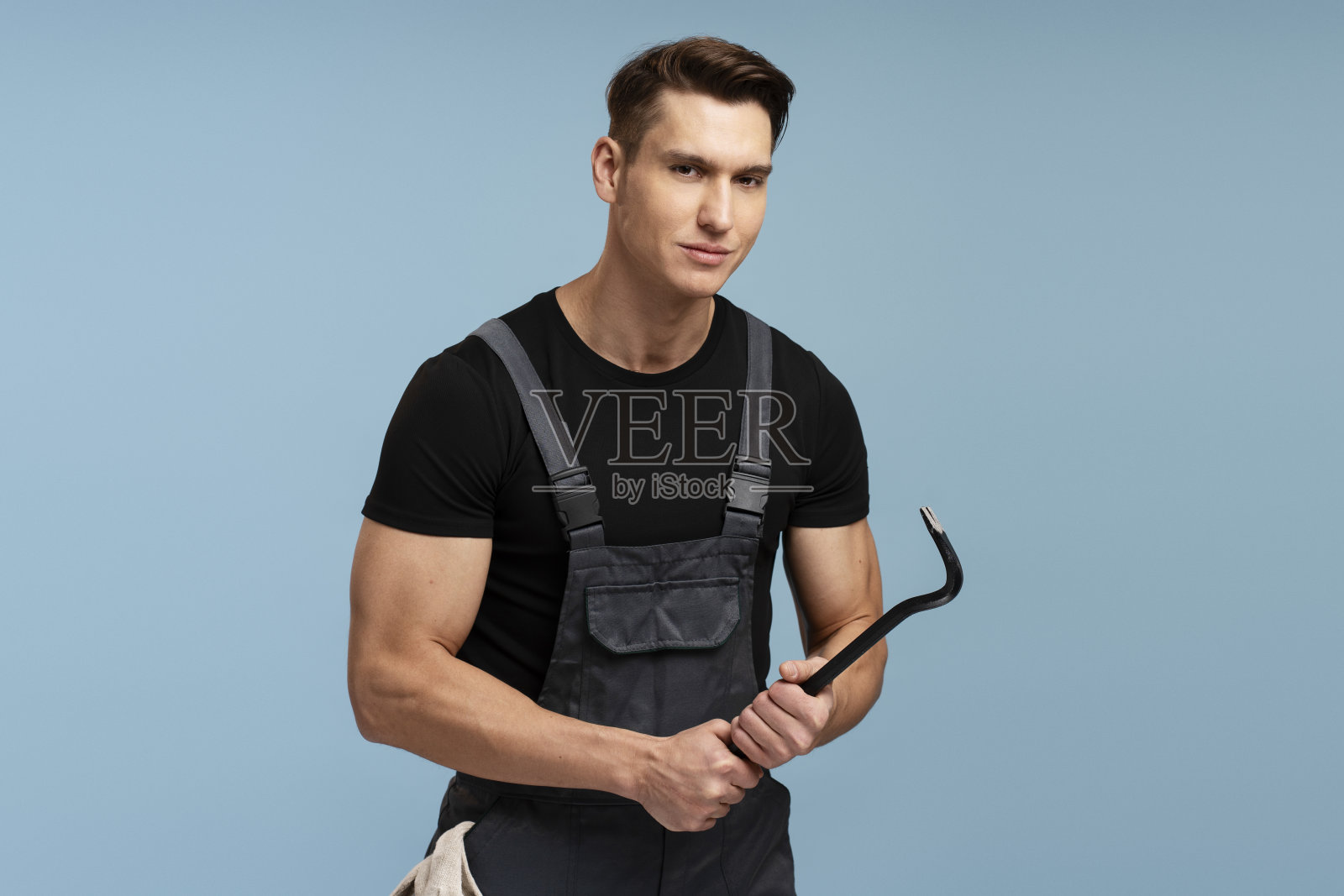 积极的男性建造者持有铁撬隔离在蓝色背景照片摄影图片