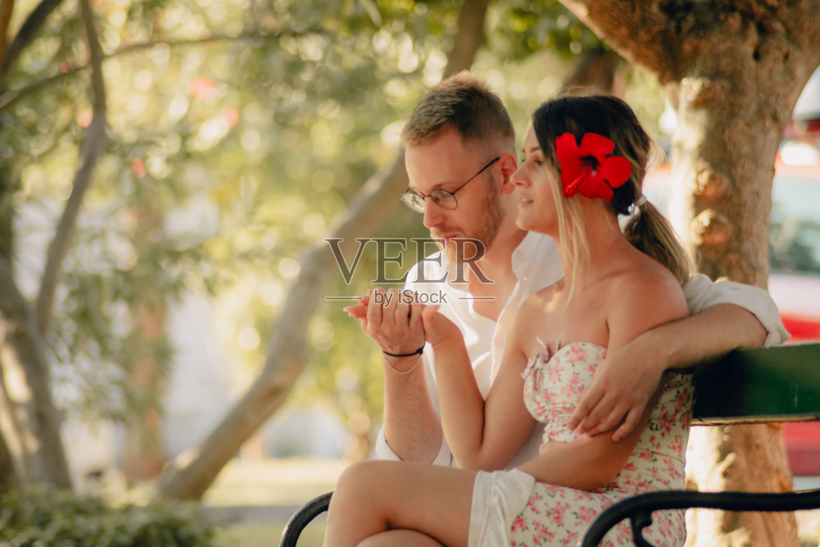 年轻的男人看着他美丽的女朋友的手,而他们正坐在公园的长椅上照片摄影图片