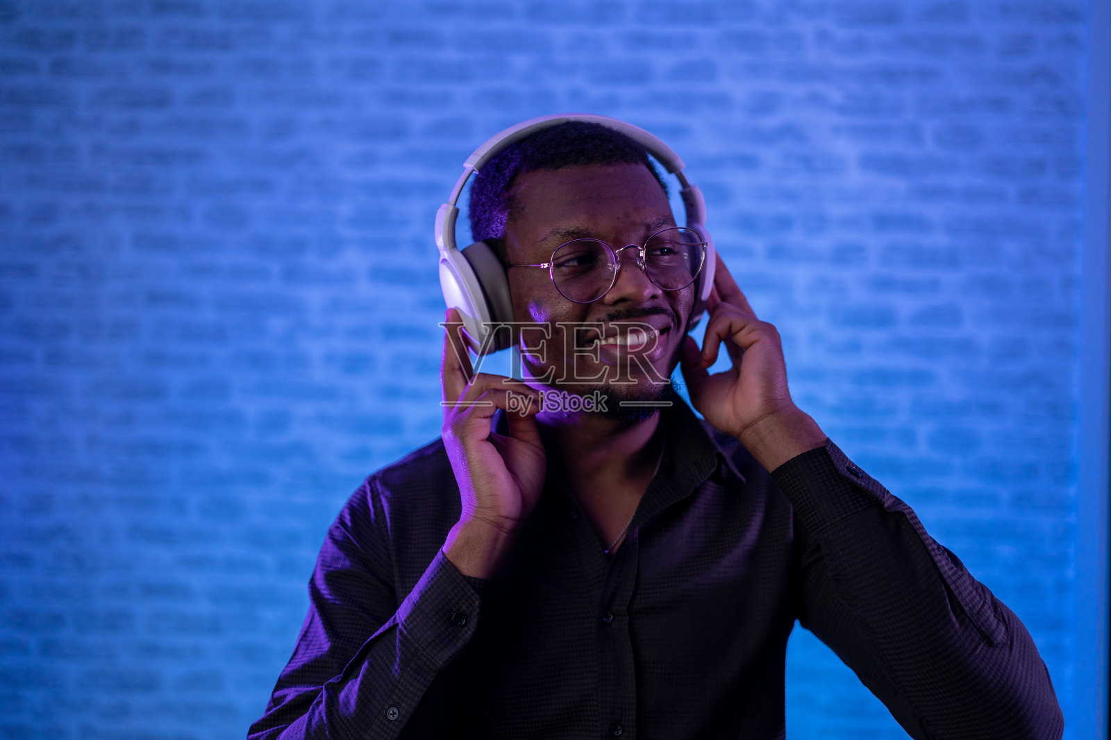 年轻英俊的黑人男子在霓虹灯的照耀下,戴着耳机听音乐照片摄影图片