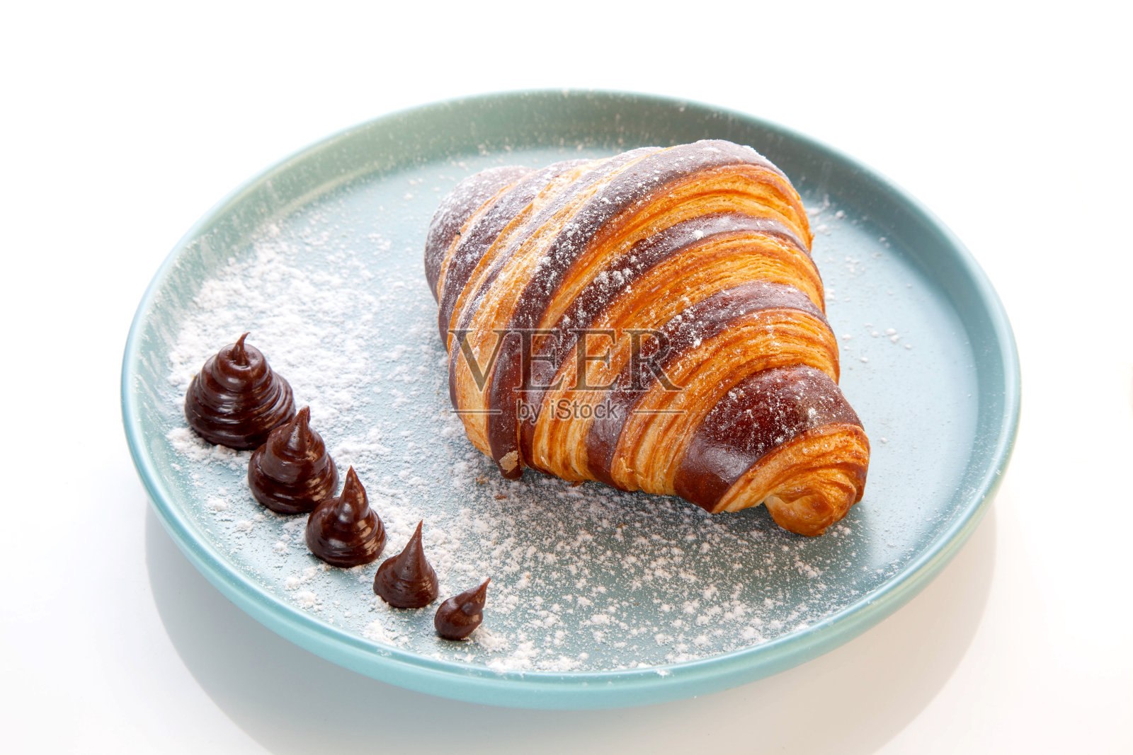 奶油蛋糕巧克力羊角包放在蓝色盘子里。照片摄影图片