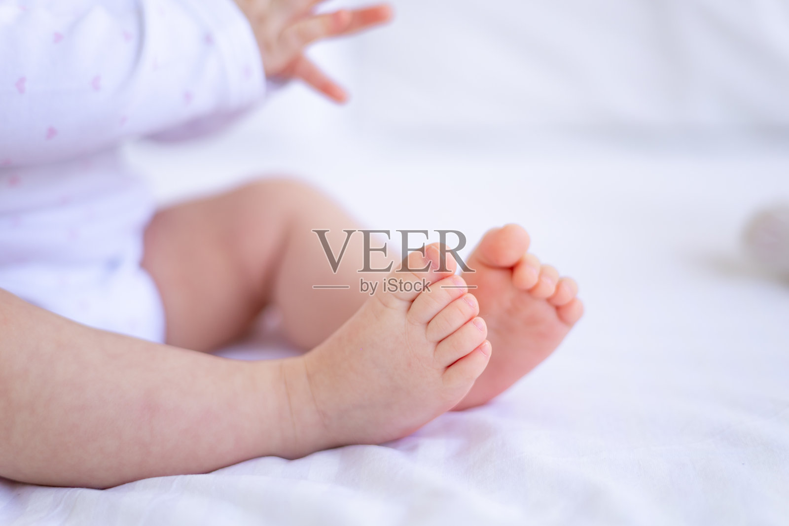 小婴儿的腿或脚躺在家里白色棉床上的婴儿床上,穿着粉红色的婴儿高跟鞋照片摄影图片