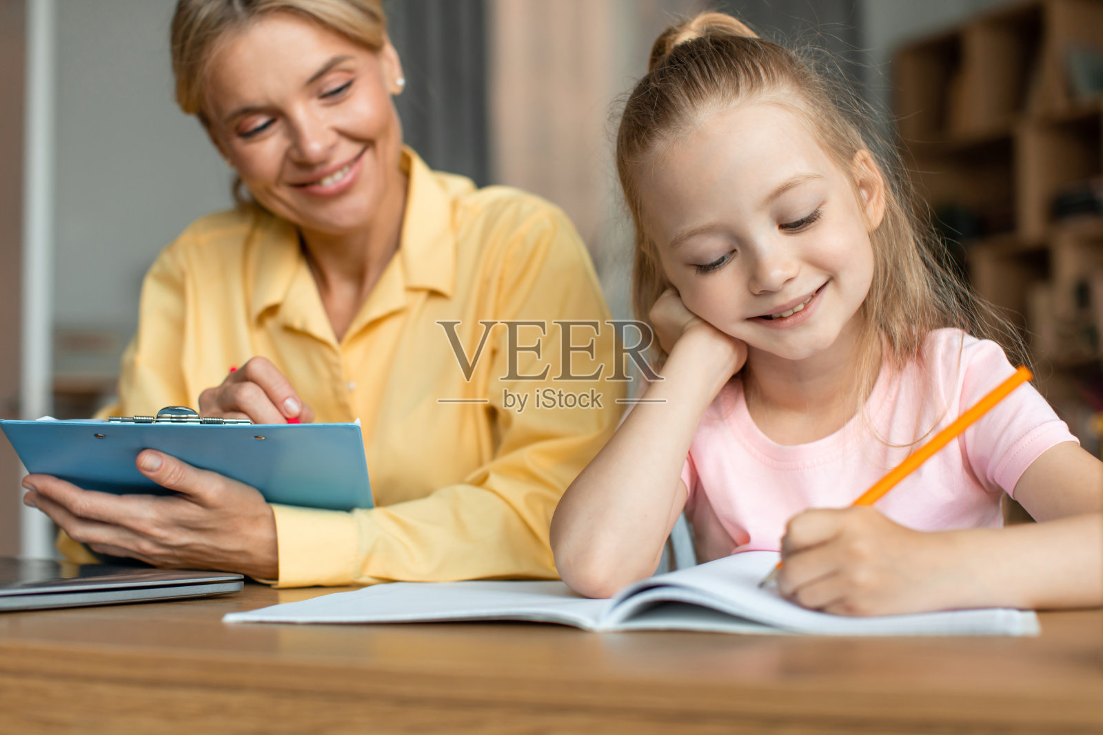 儿童发展学校。专业的女语言教师与女孩一起锻炼,聪明的孩子在抄写本照片摄影图片