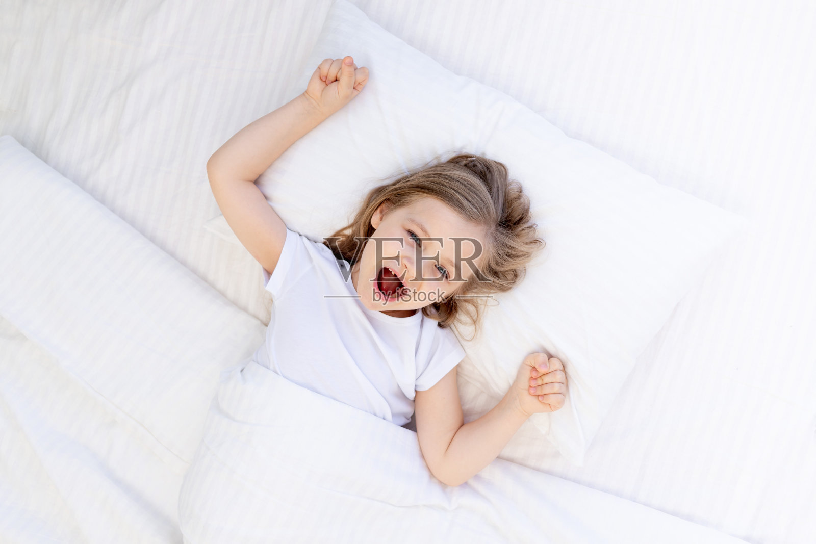 甜甜地打哈欠的女婴睡在床上,白色的棉枕上盖着毯子,宝宝晚上睡得很健康照片摄影图片