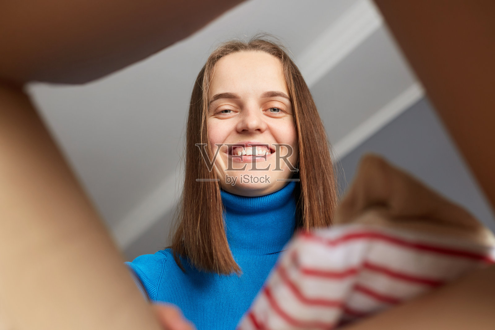 搬迁搬迁包装材料。穿着蓝色高领毛衣的微笑女人打开包裹,从公寓搬到新家后,从纸板箱里打开衣服和东西。照片摄影图片