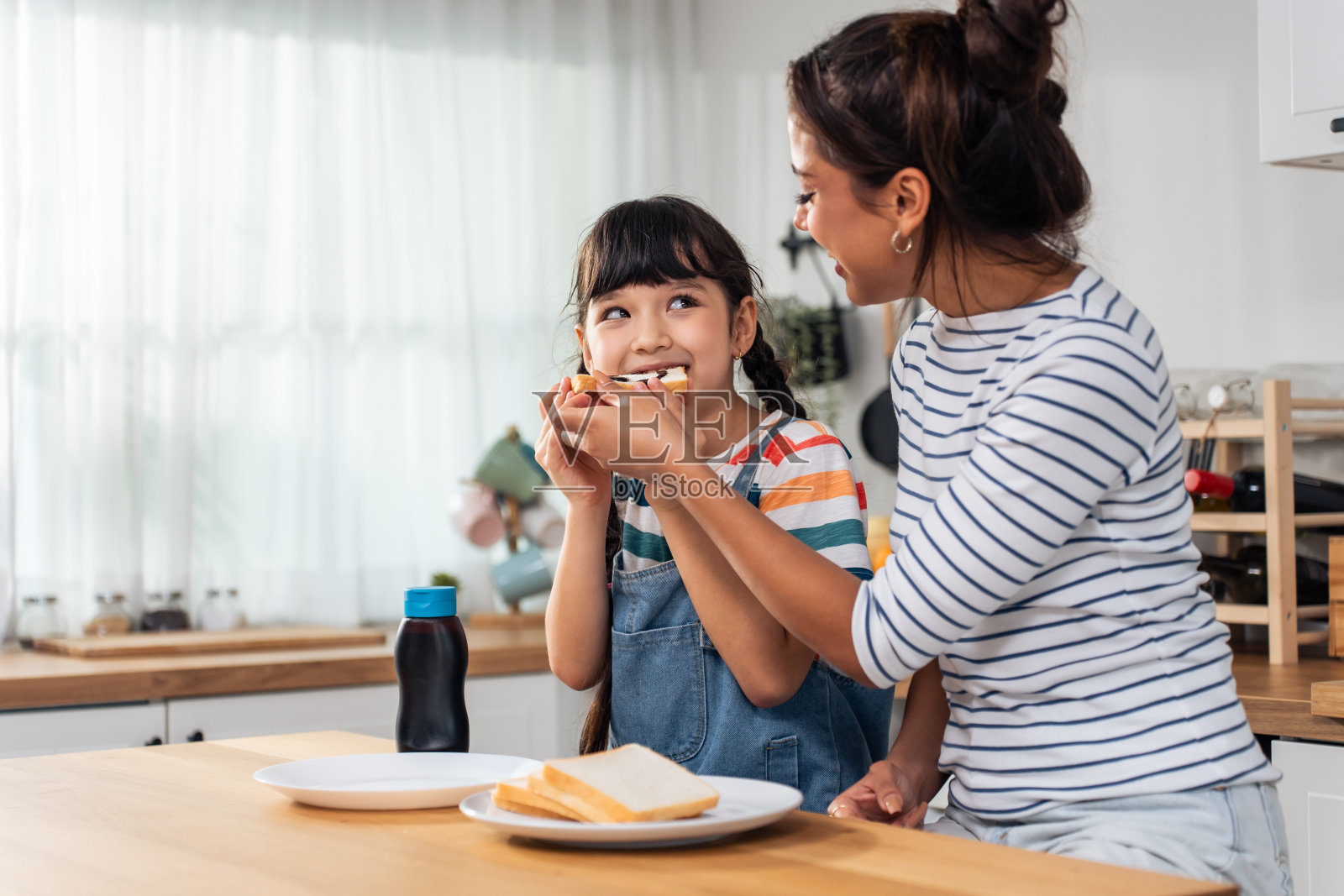 白种人幸福的家庭,父母在家陪孩子。年轻的女儿和妈妈在厨房里快乐地吃着甜蜜的巧克力和面包。住宅概念中的活动关系照片摄影图片
