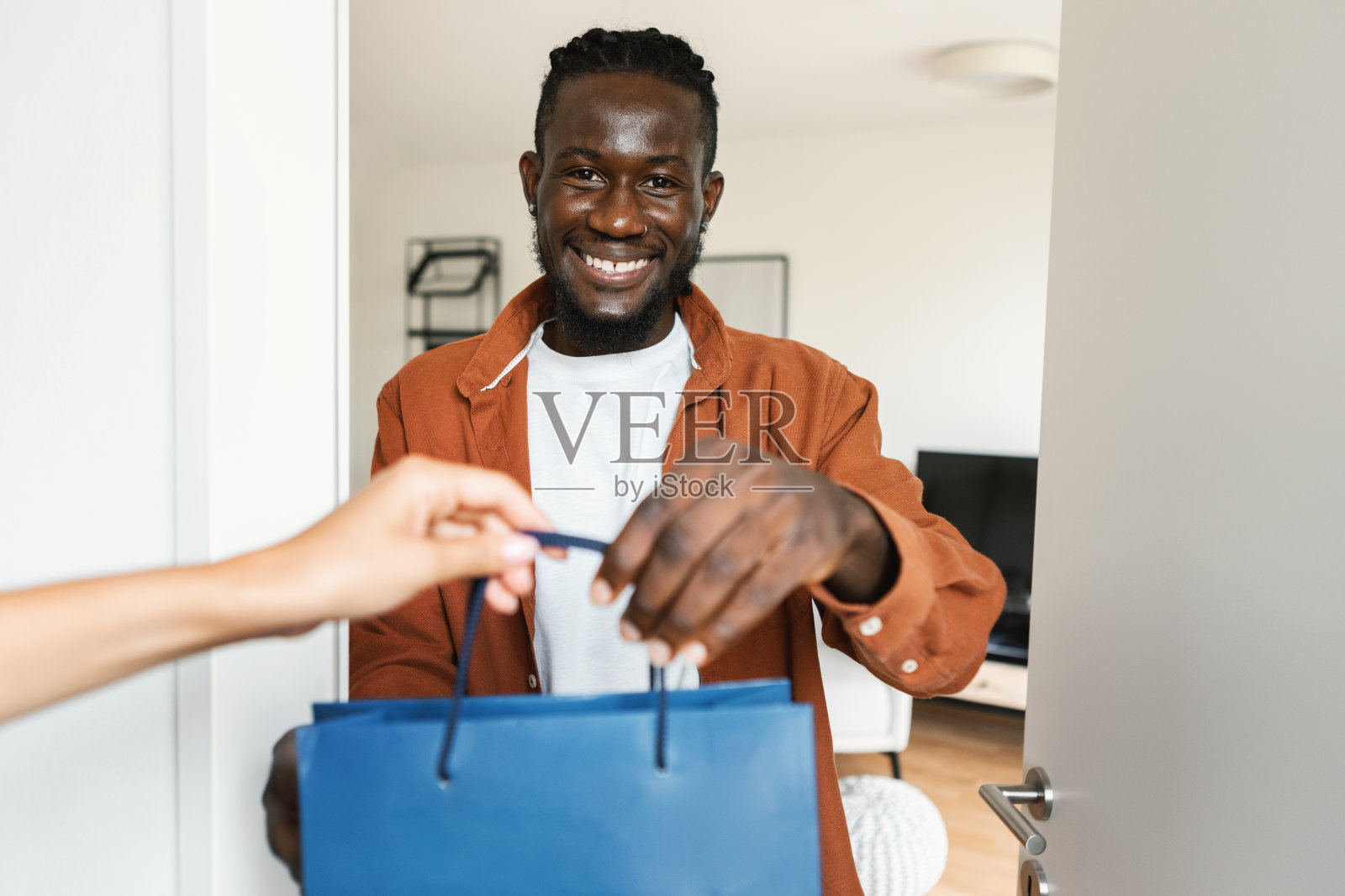 购物送货服务。快乐的非洲裔美国人从快递员那里得到购物袋,对着镜头微笑照片摄影图片