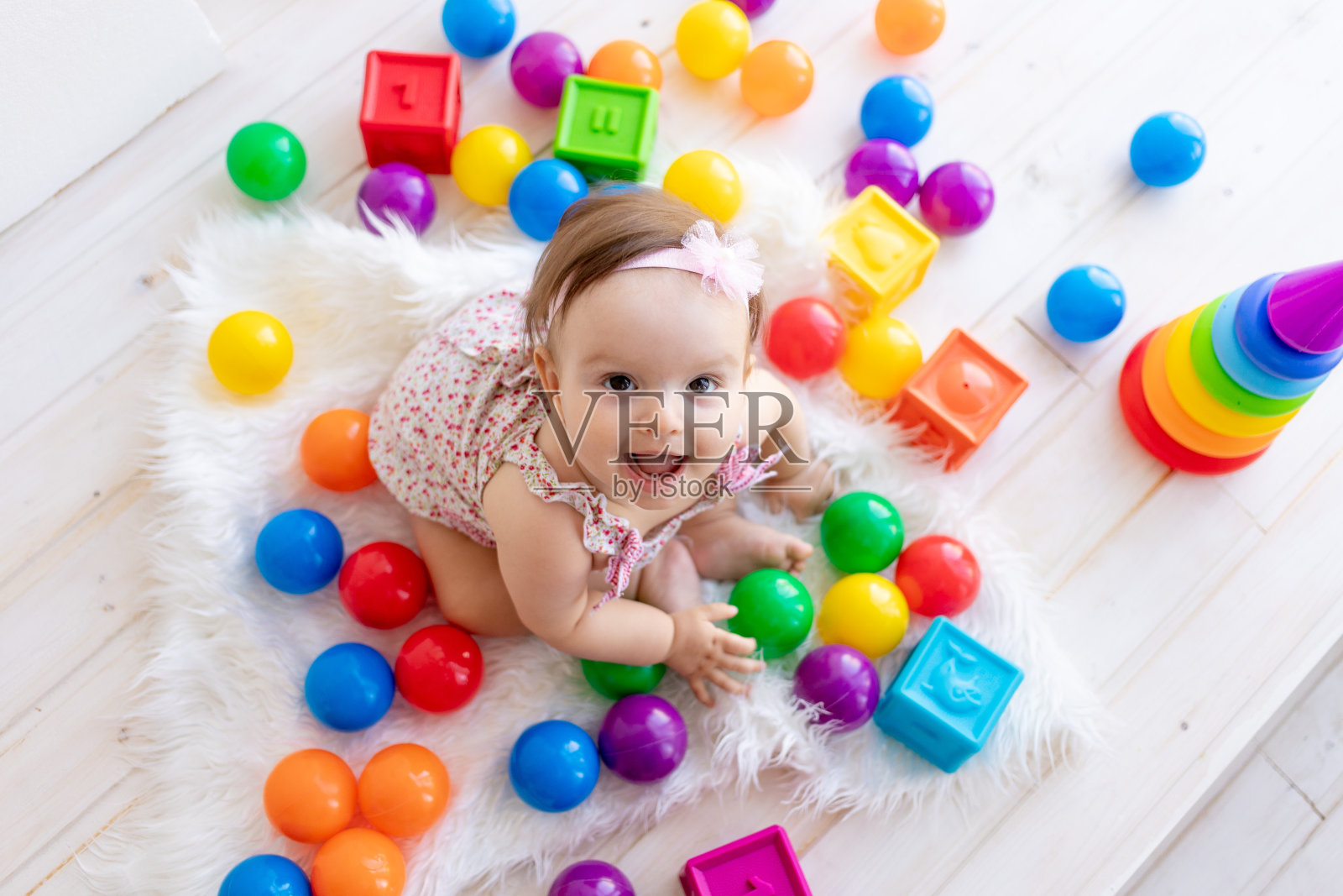 快乐的小女孩坐在一间白色的房间里,穿着一件红色的裙子,里面有鲜艳的玩具,看着上面照片摄影图片