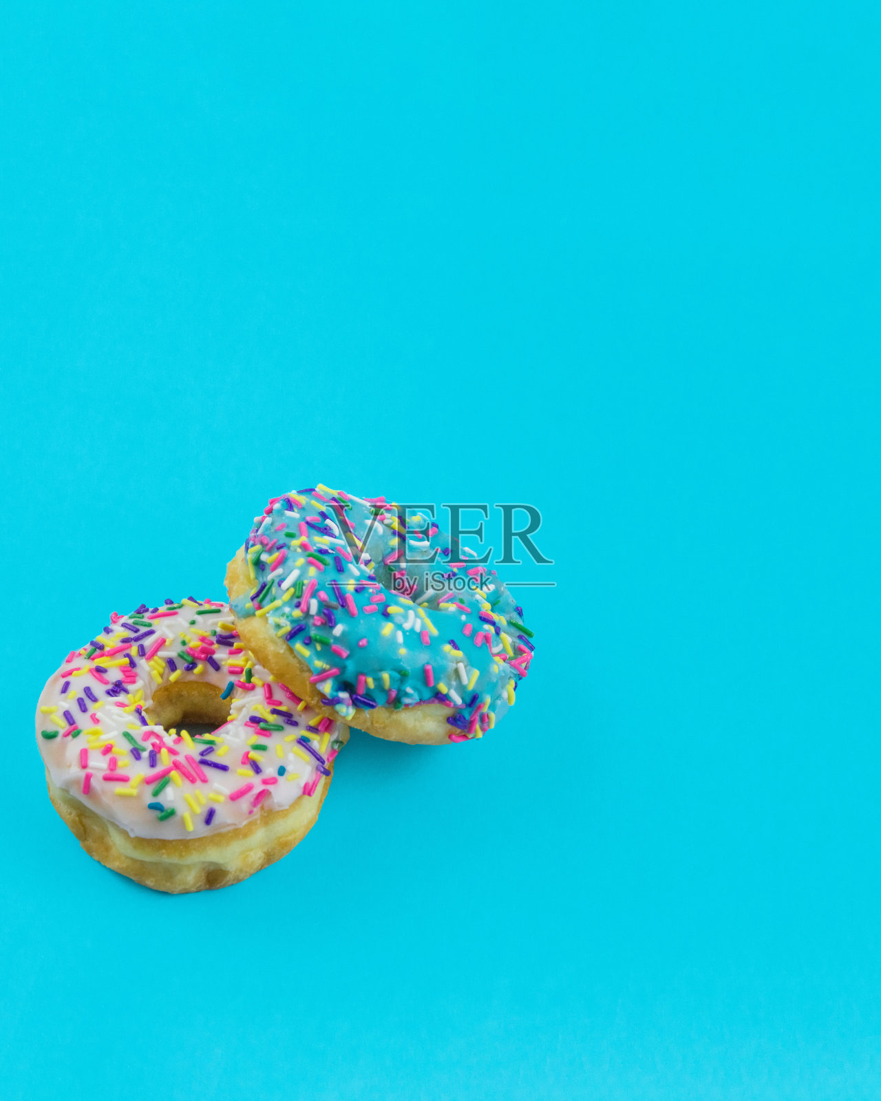 两个甜甜圈,糖衣和撒糖在一个简单的蓝色背景复制空间照片摄影图片