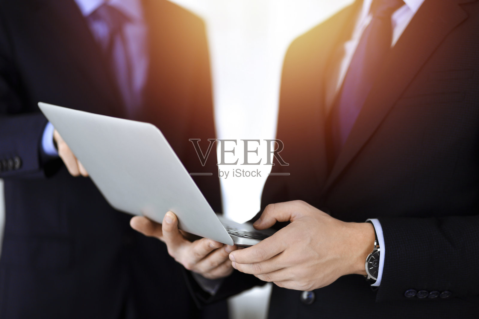 商务人士站在阳光明媚的现代办公室里,在会议上讨论演示文稿。不知名的商人和同事在笔记本电脑上搜索一些信息,律师在谈判。团队合作及伙伴关系理念照片摄影图片