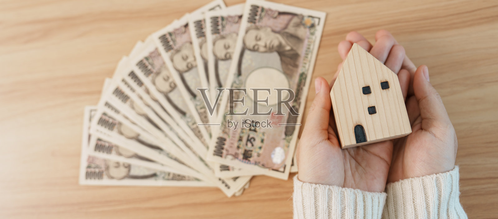 女人拿着日元钞票和房子模型。房地产,住房,抵押贷款,日本现金,税收,经济衰退,通货膨胀,投资,金融和储蓄的概念照片摄影图片