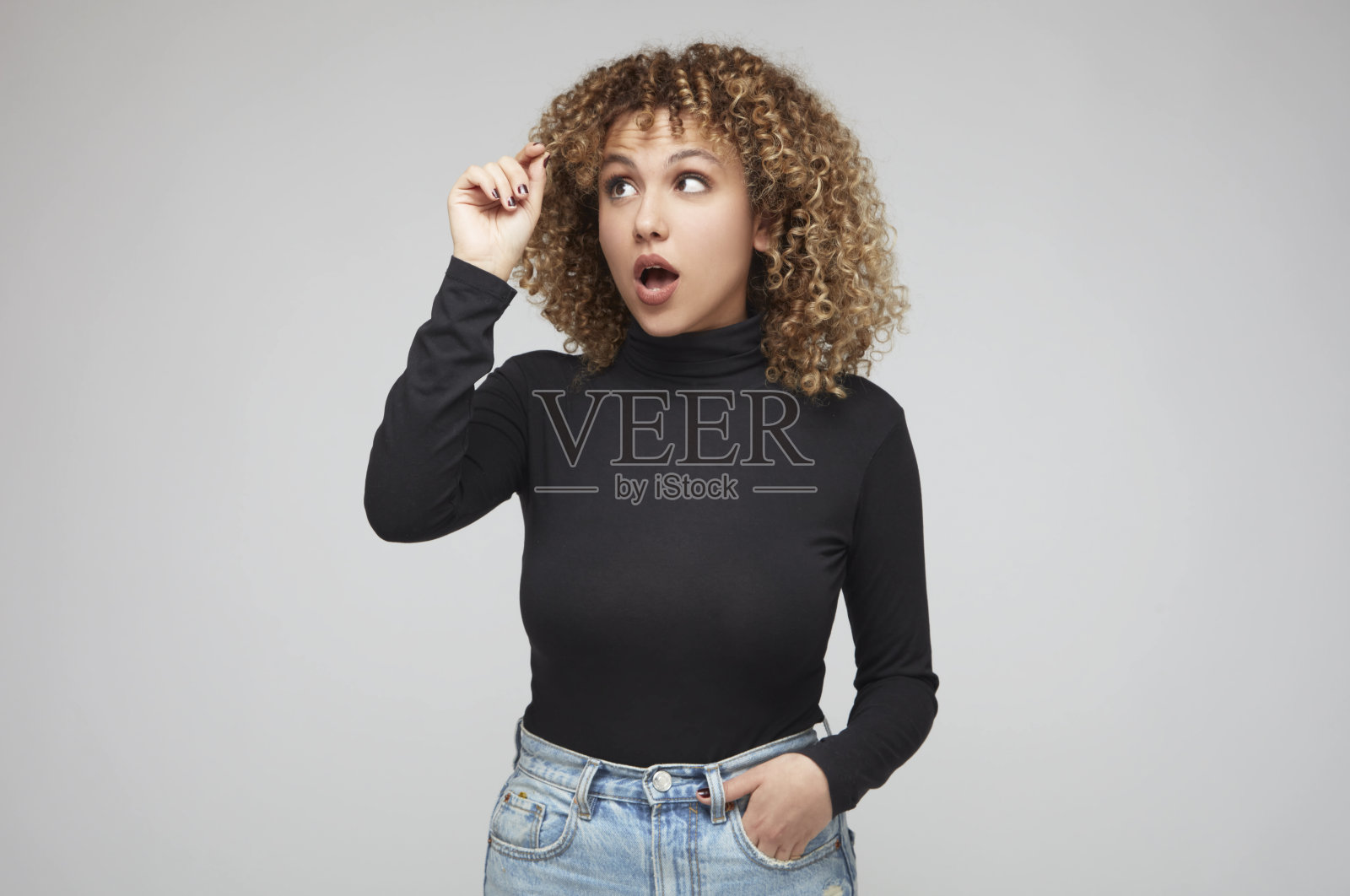 年轻女子拿着一绺卷发,惊讶地看着它。照片摄影图片