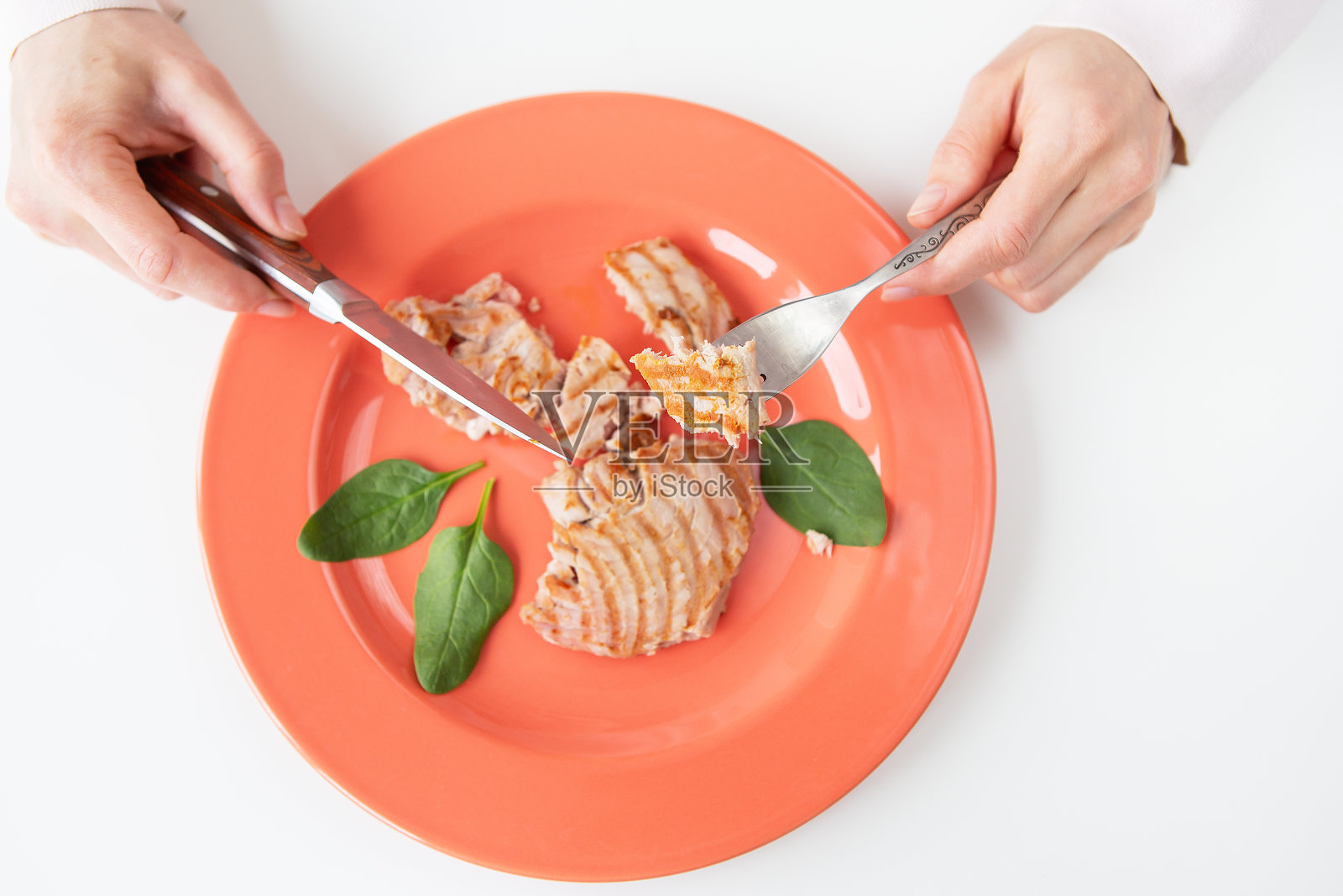 一个多汁美味的烤金枪鱼牛排在明亮的珊瑚盘特写镜头。美味健康,营养合理。这个女孩拿着刀叉。从上面看。照片摄影图片