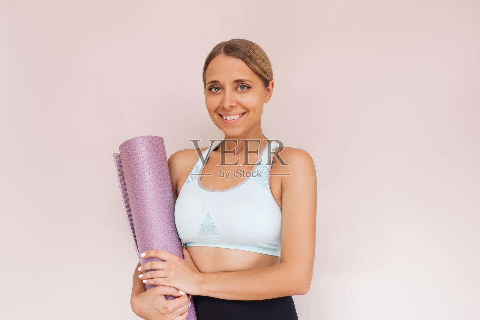 一个年轻的白人微笑适合晒黑的金发女人拿着瑜伽垫在她的手中照片摄影图片