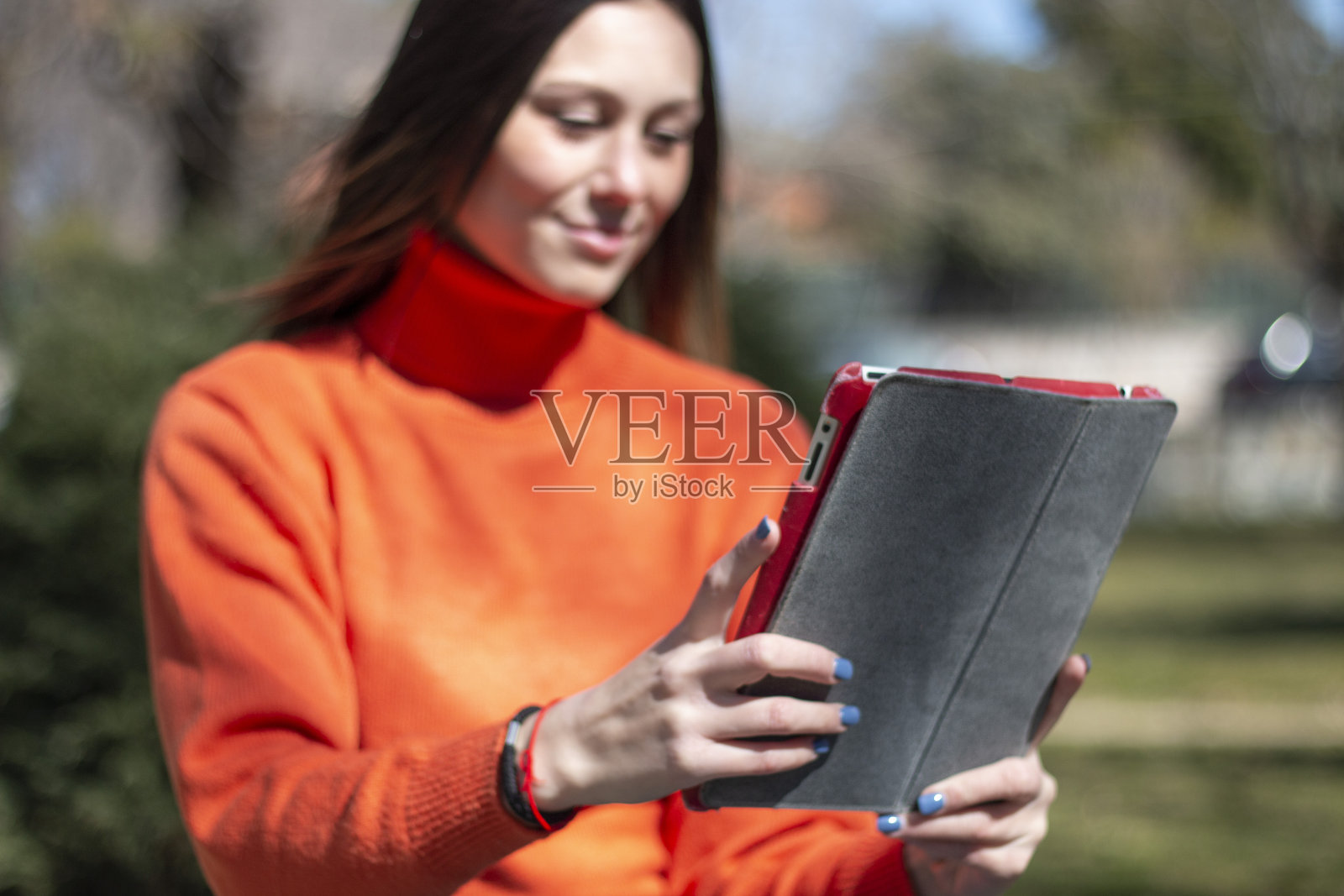 年轻的黑发女子坐在公园的草地上摆弄着平板电脑或电子设备照片摄影图片