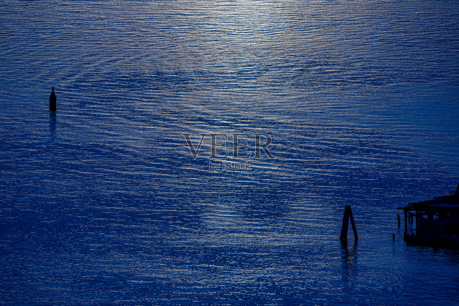 在落日余晖中,浮标和杆子标志着航路。照片摄影图片