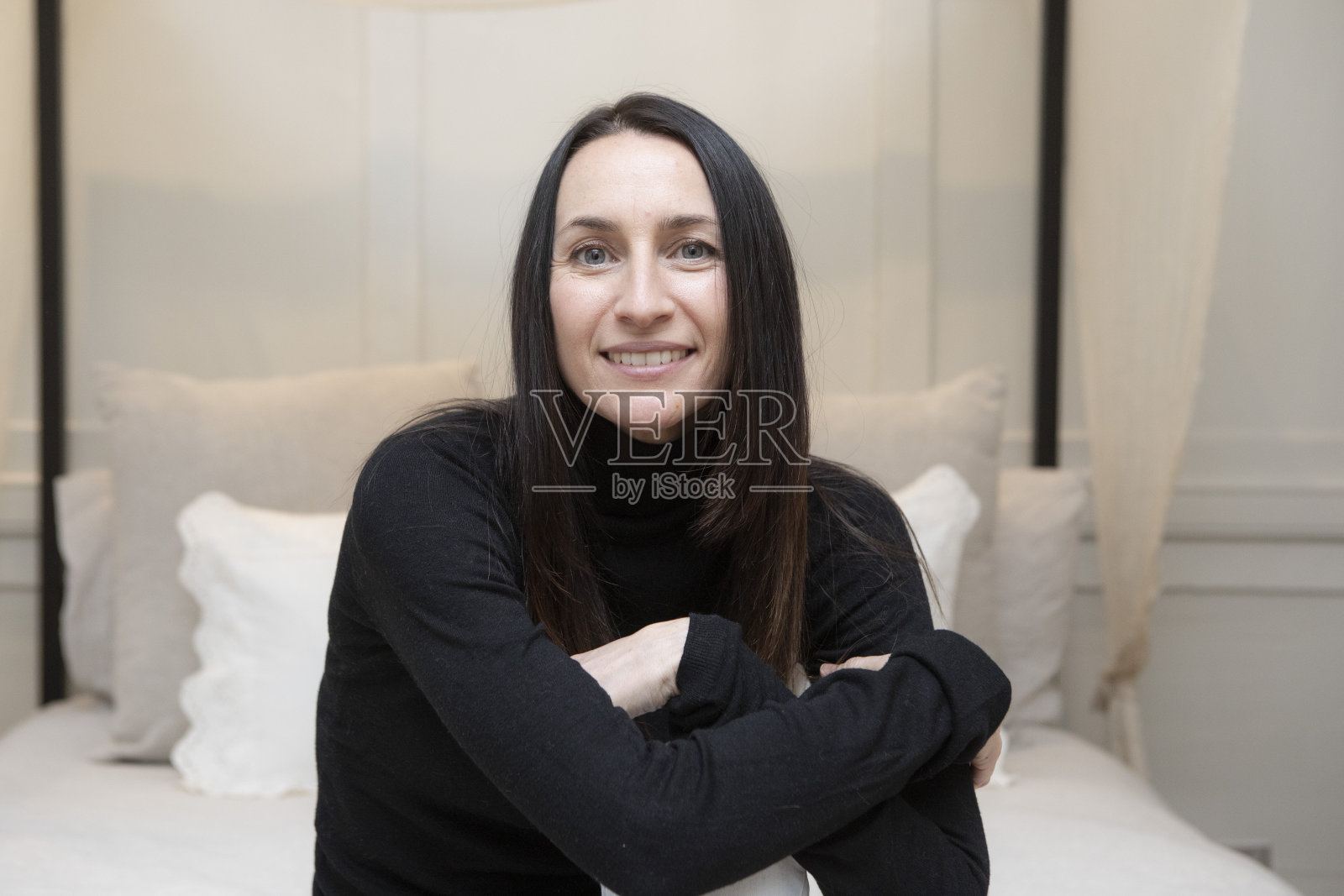 一个迷人的女人双臂交叉坐在四柱床上的肖像照片摄影图片