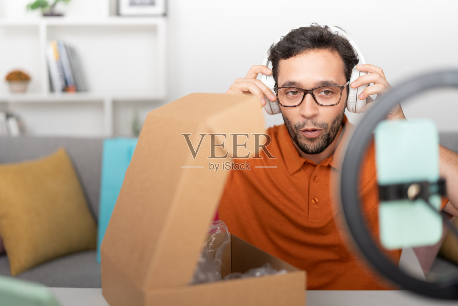 一名年轻男子用他的新耳机在他的社交网络上用手机在一圈光中录制视频。照片摄影图片