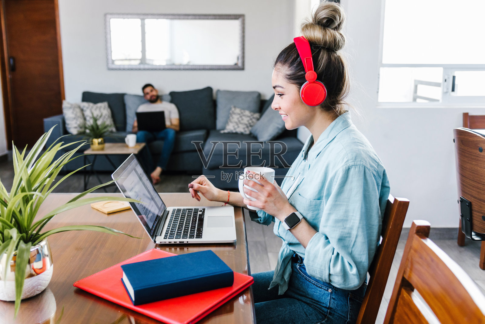 年轻的拉丁女人在墨西哥的家里戴着耳机在笔记本电脑上工作,西班牙人的家庭办公室照片摄影图片
