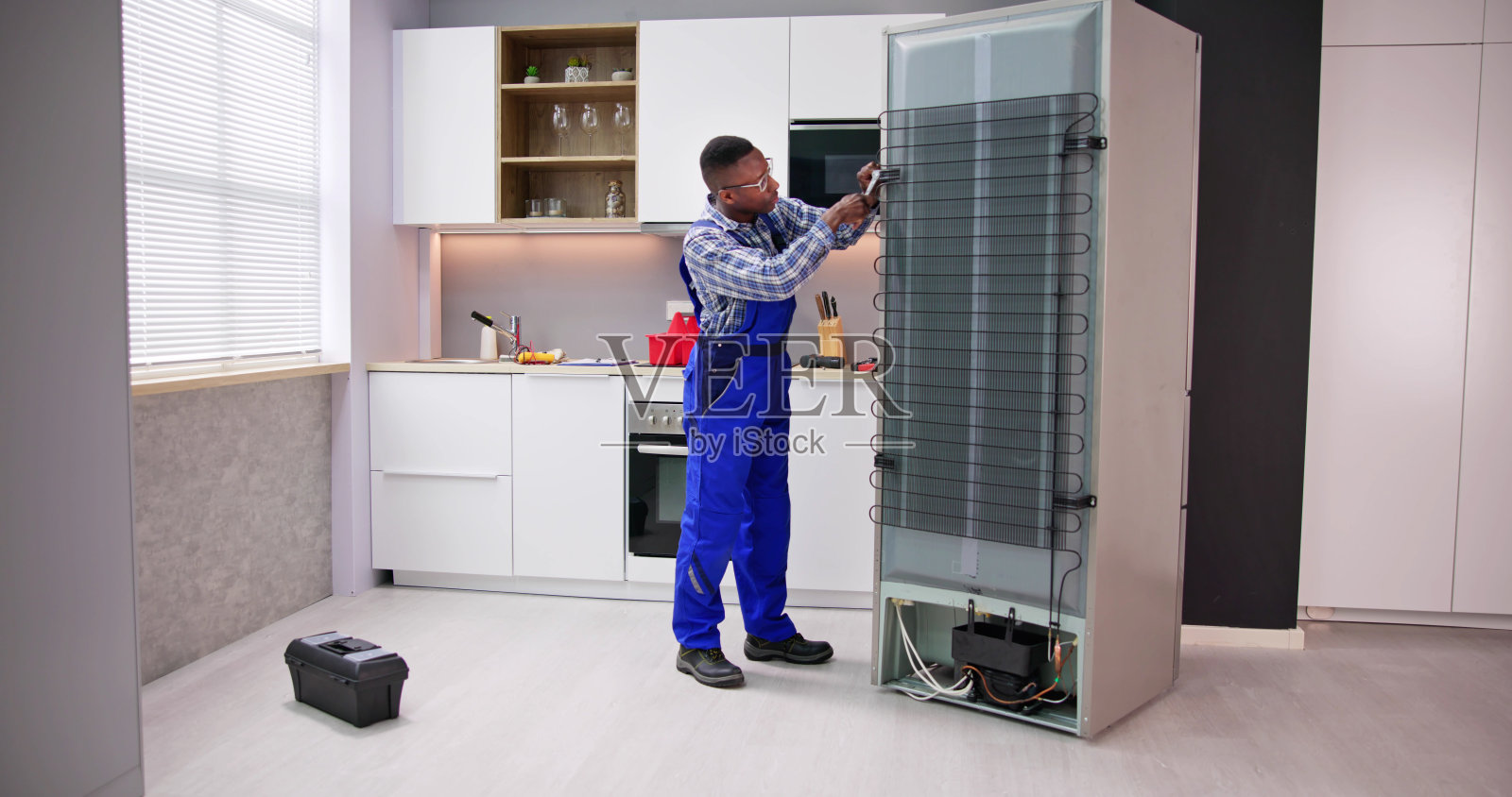 年轻的男军人正在用螺丝刀修理冰箱照片摄影图片