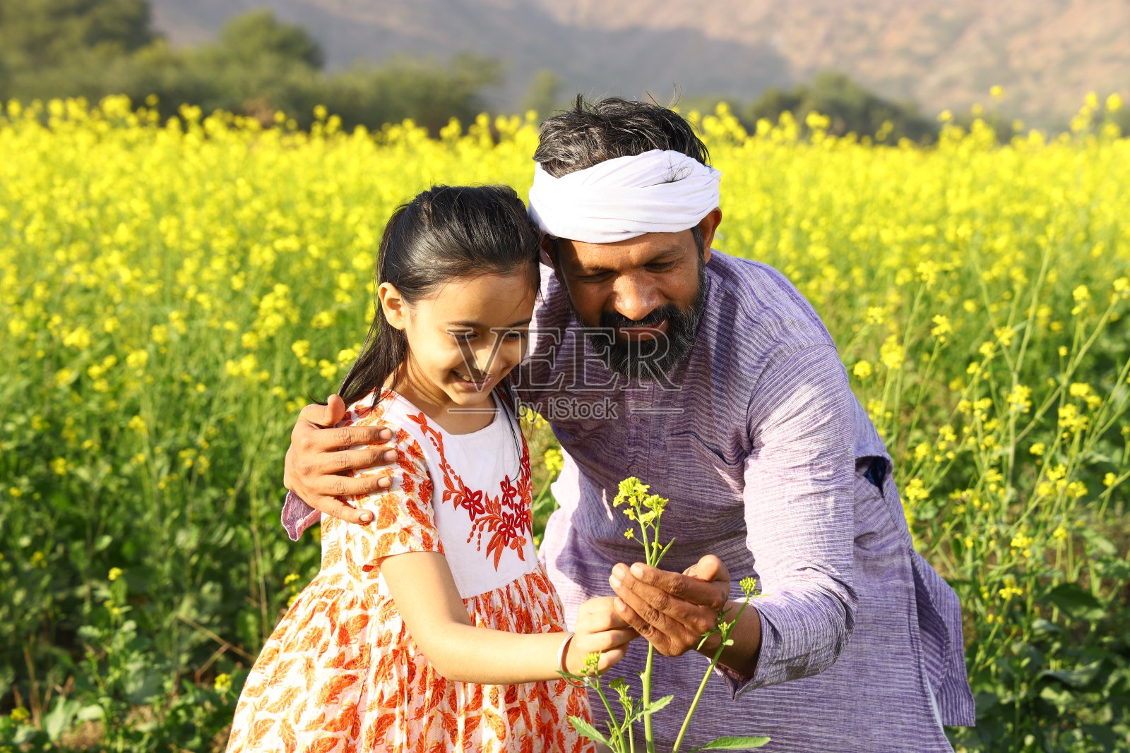 快乐的印度农民和他的女儿坐在一起,给她看一朵美丽的花。照片摄影图片