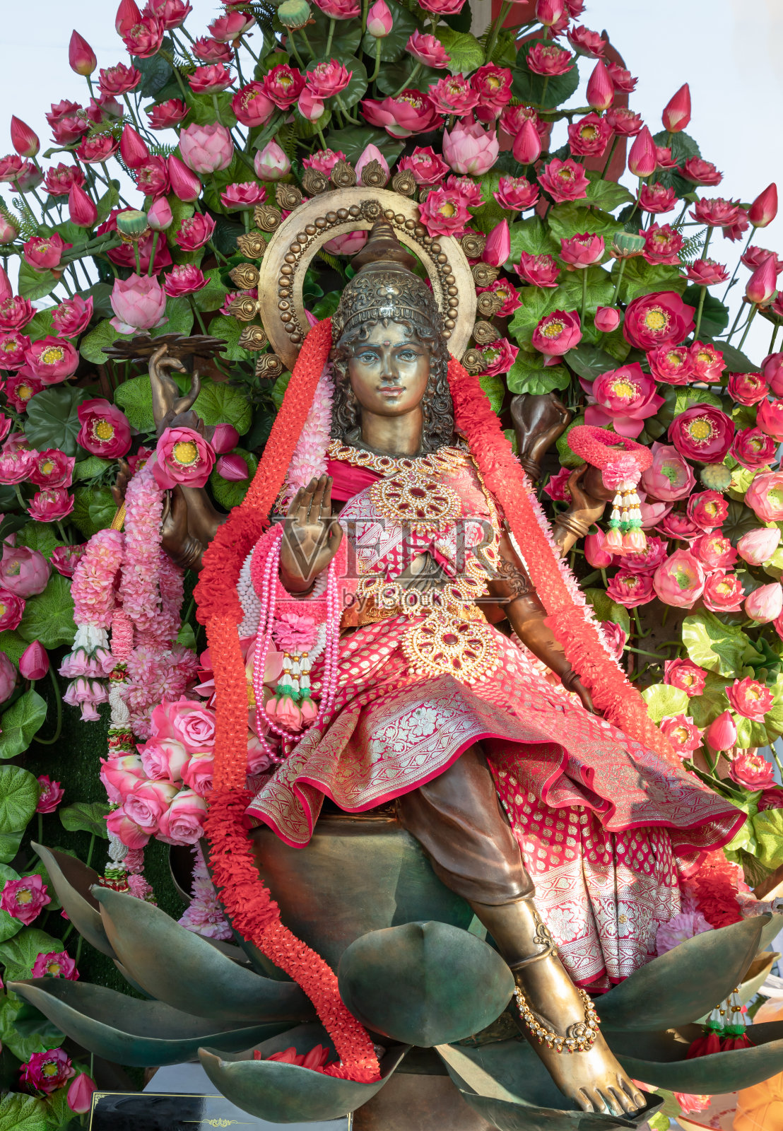 黄铜印度女神拉克希米(玛哈拉克希米)的雕像装饰着花环和粉红色的莲花花束。照片摄影图片
