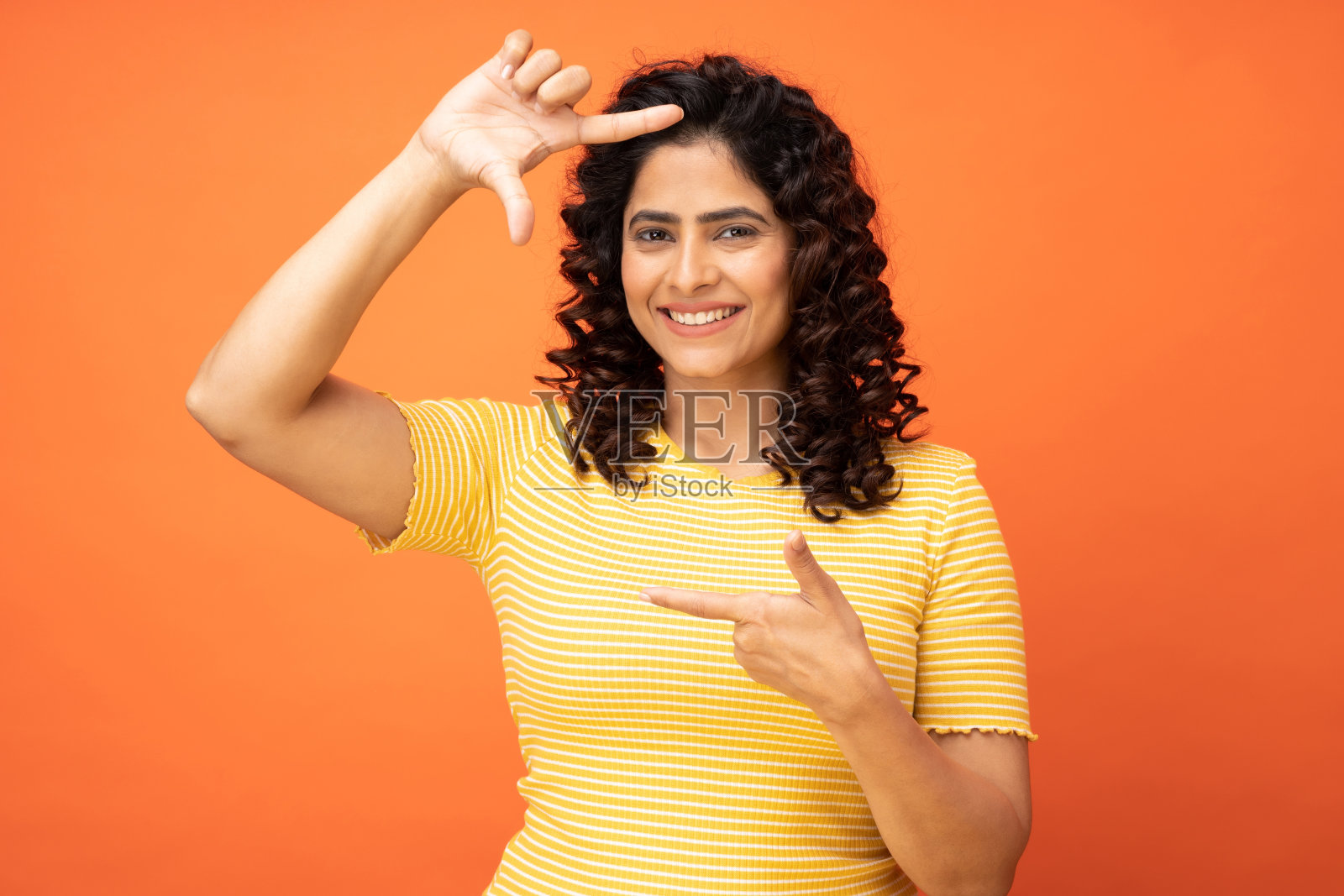 有吸引力的漂亮的现代漂亮卷发快乐的年轻女子显示与框架手势隔离在明亮的橙色背景,股票照片照片摄影图片