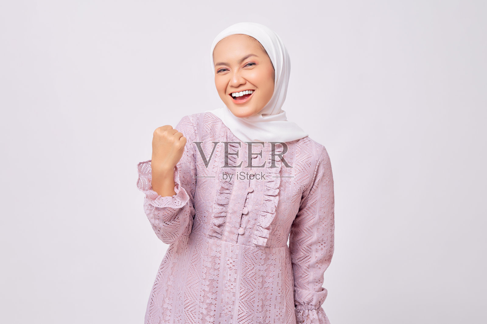 兴奋的美丽年轻的亚洲穆斯林妇女戴着头巾和紫色连衣裙举起拳头,庆祝斋月的胜利孤立在白色的工作室背景照片摄影图片