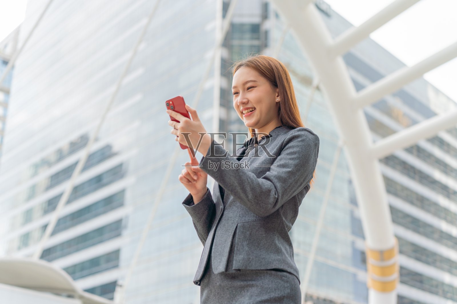 年轻的亚洲女商人,穿着灰色的办公套装,在商业区使用她的智能手机,微笑着自信照片摄影图片