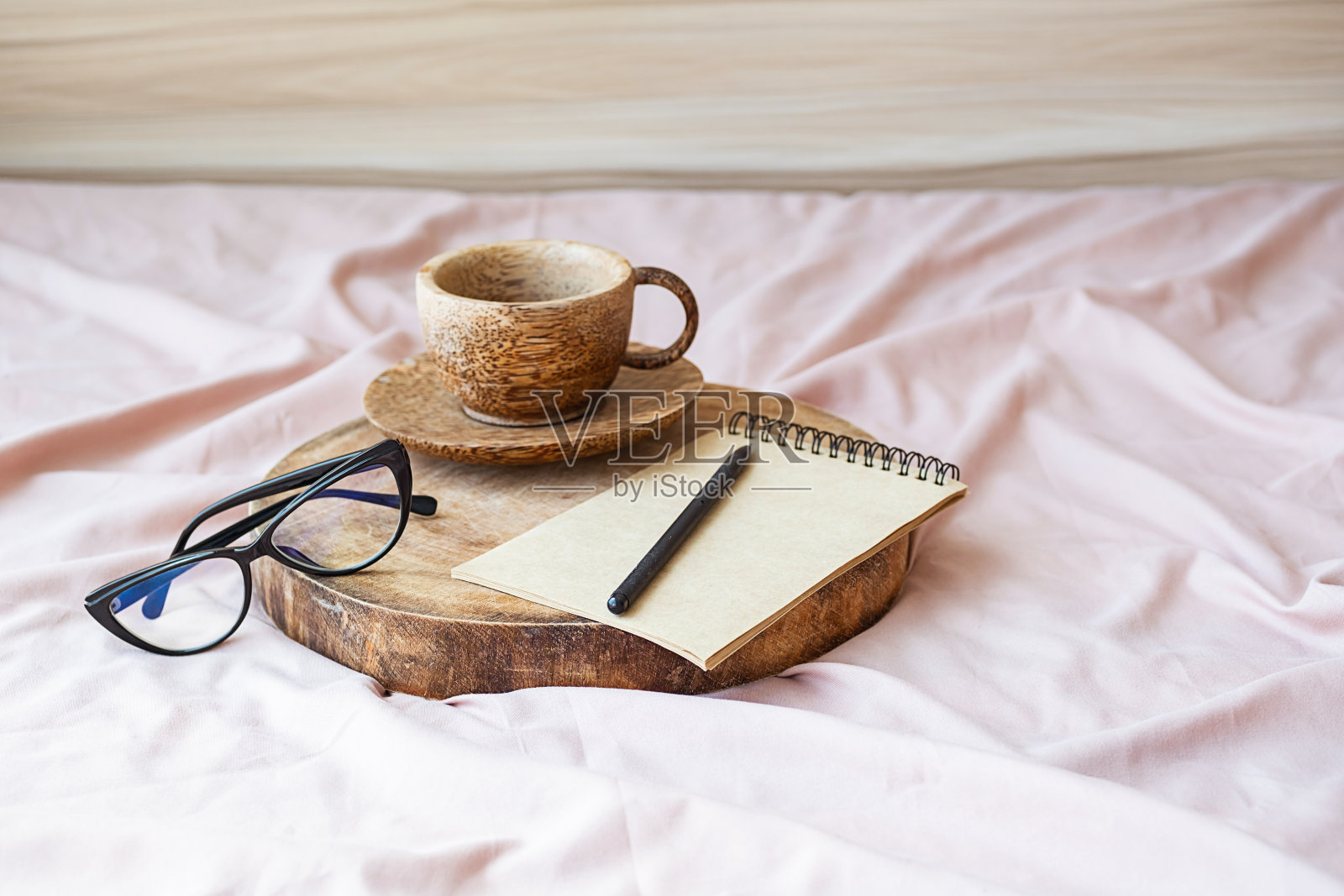 早上的咖啡杯在空白笔记本旁边,护目镜在被单上的木托盘上。照片摄影图片