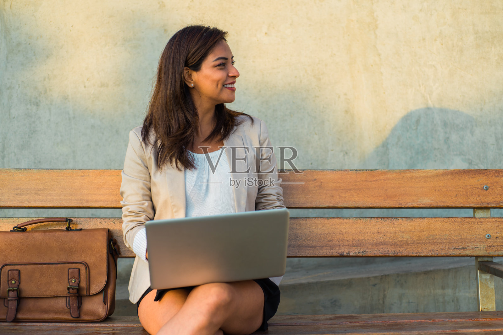 一位坐在长椅上拿着电脑的拉丁妇女微笑着看着复印区。照片摄影图片