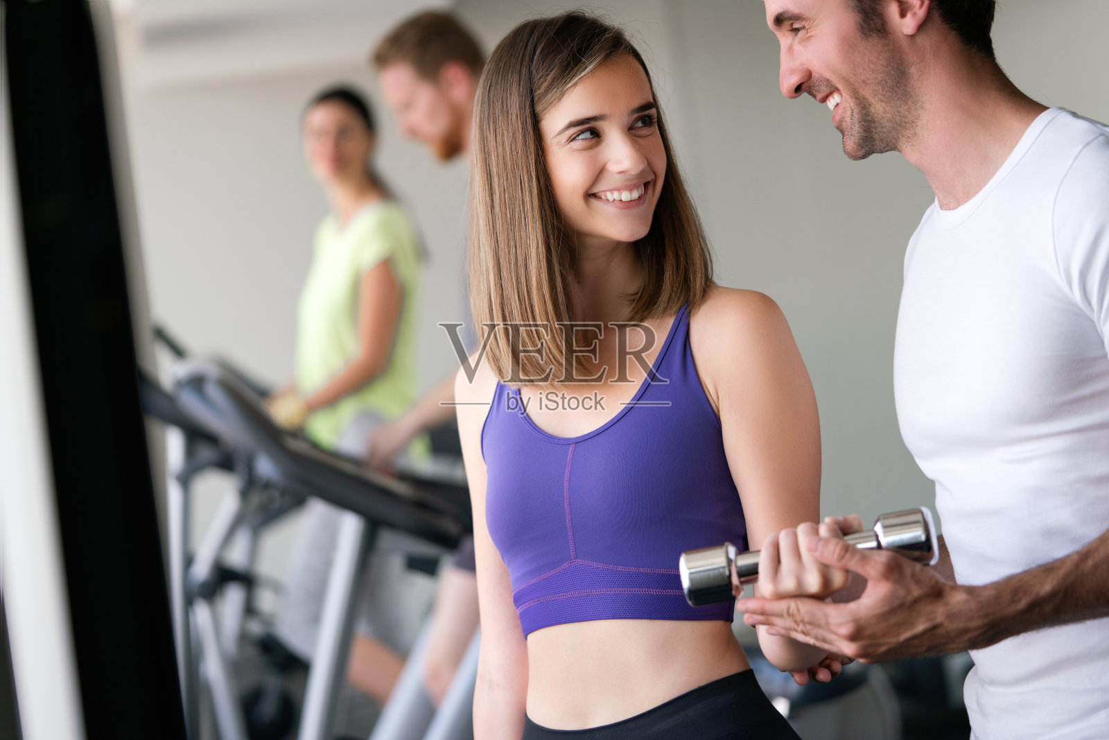 美丽的女人在健身房用哑铃做练习。女孩正在享受她的训练过程照片摄影图片