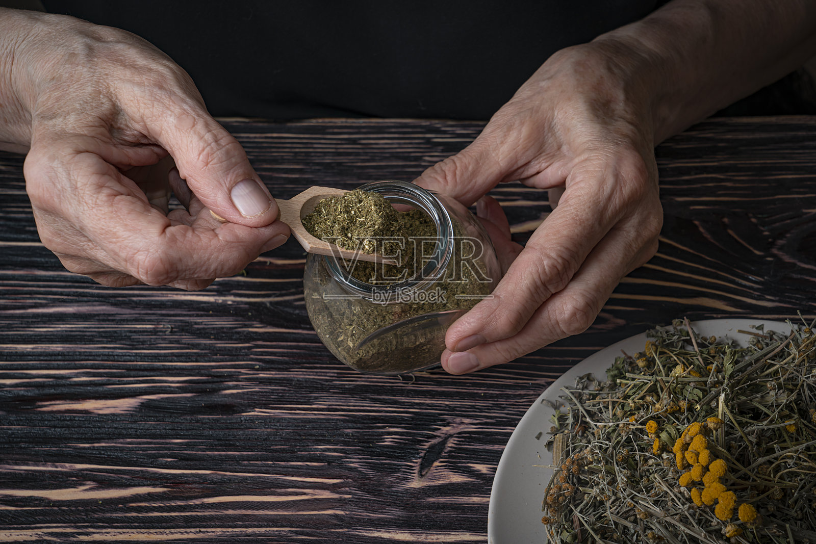 干药材,抗寄生虫收集的丁香,艾草和丁香。草药医生把碾碎的草药倒入罐子里。照片摄影图片