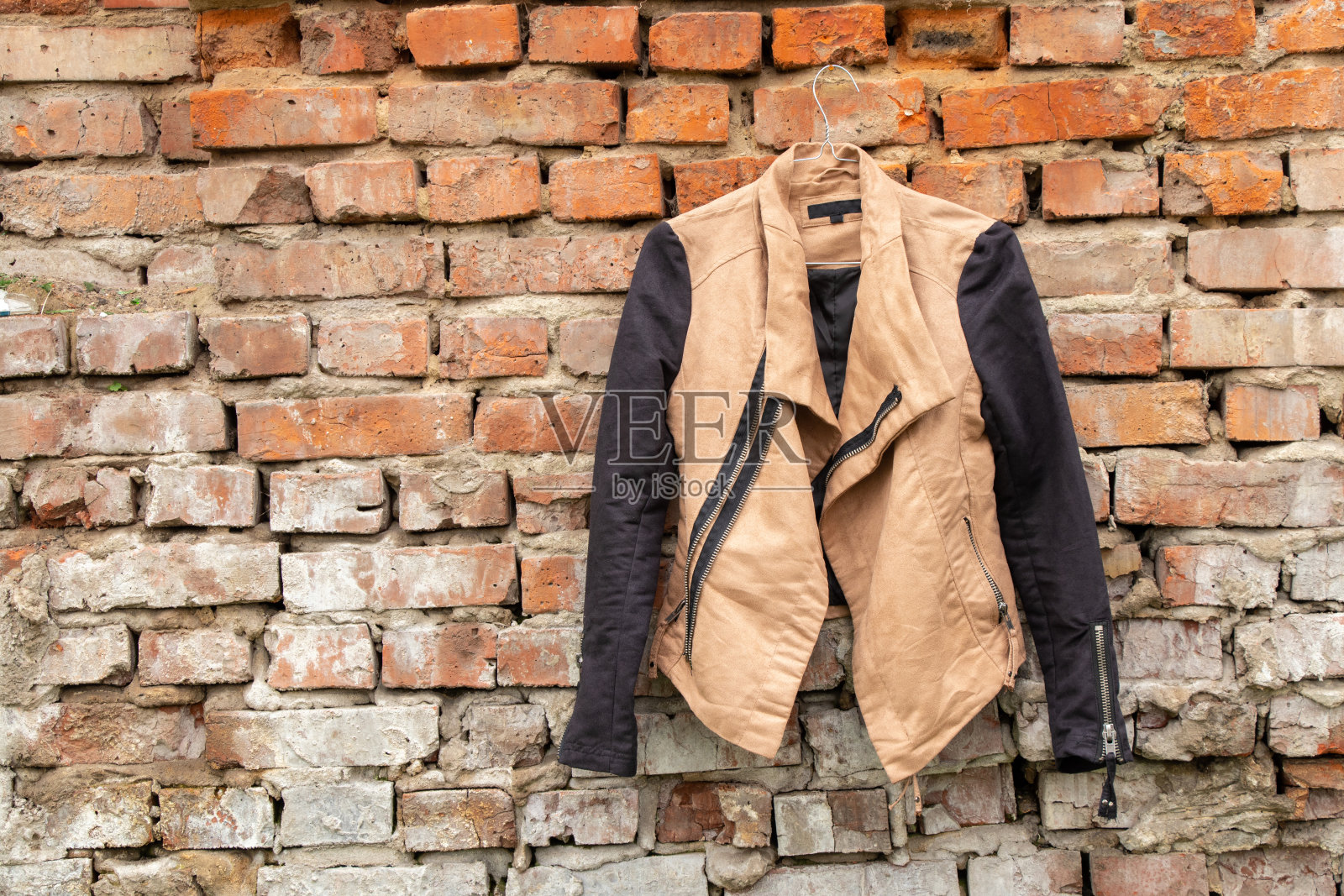 棕色女子夹克衫挂在街上自家砖墙上的衣架上,时尚照片摄影图片